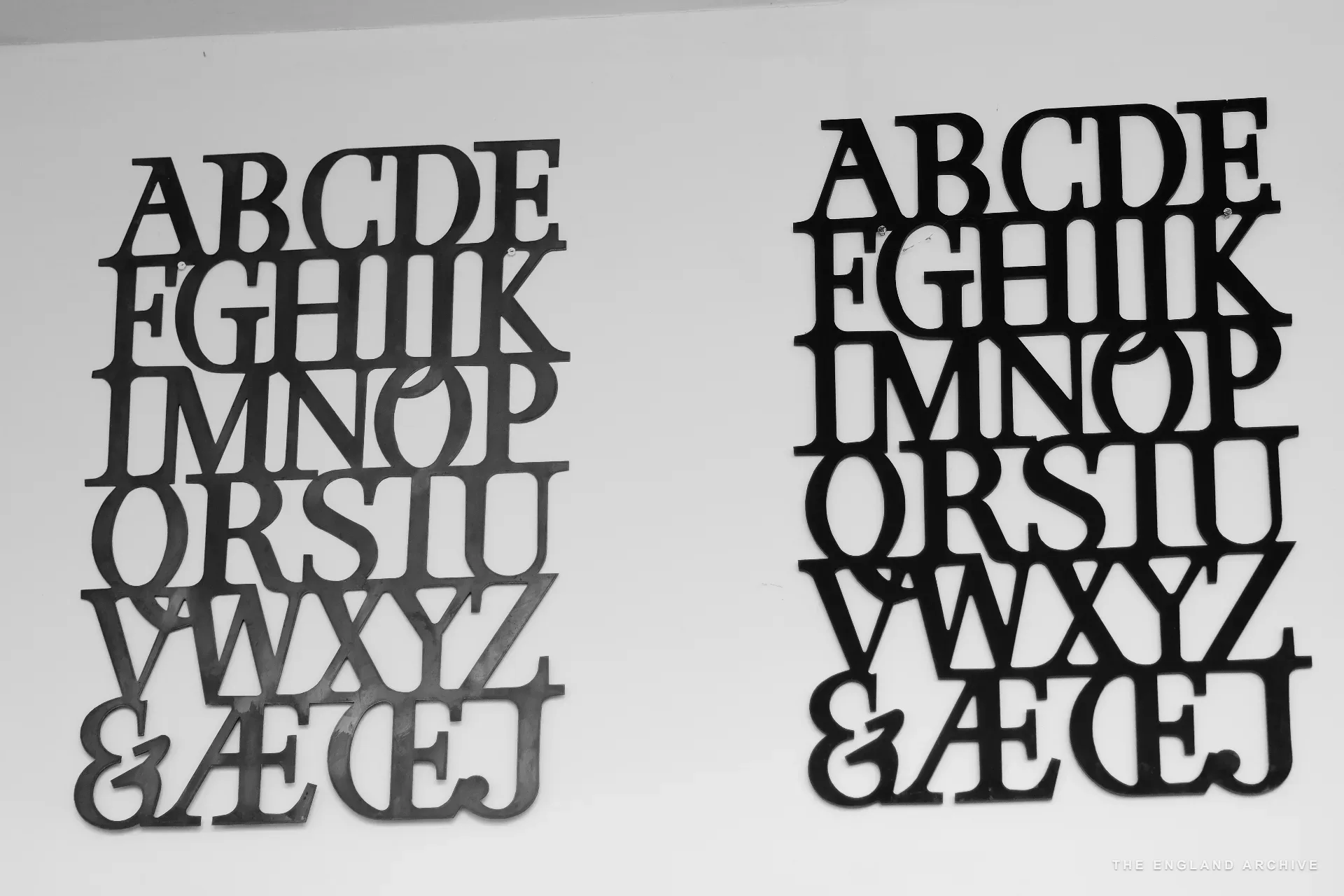 Two large alphabet panels mounted side by side on the workshop's white wall - the letterforms cut out of black material in the workshop's house style, A through Z plus an ampersand and ligatures.
