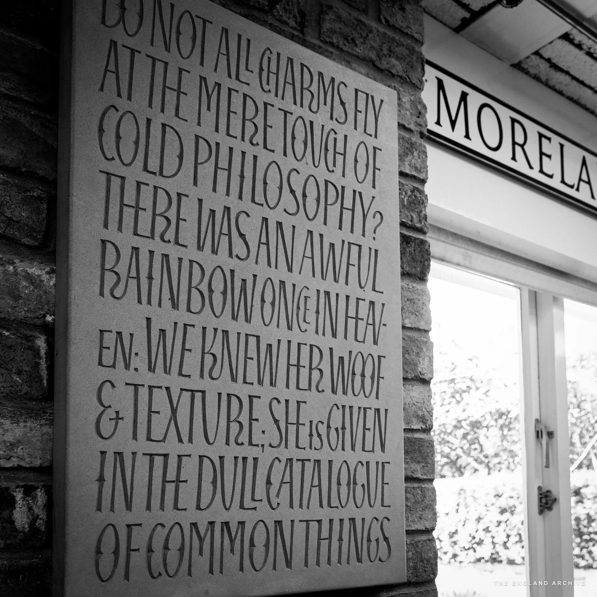 A large slate panel mounted on a brick wall, deeply cut with a Keats verse: 'Do not all charms fly at the mere touch of cold philosophy? There was an awful rainbow once in heaven: we knew her woof & texture; she is given in the dull catalogue of common things.'