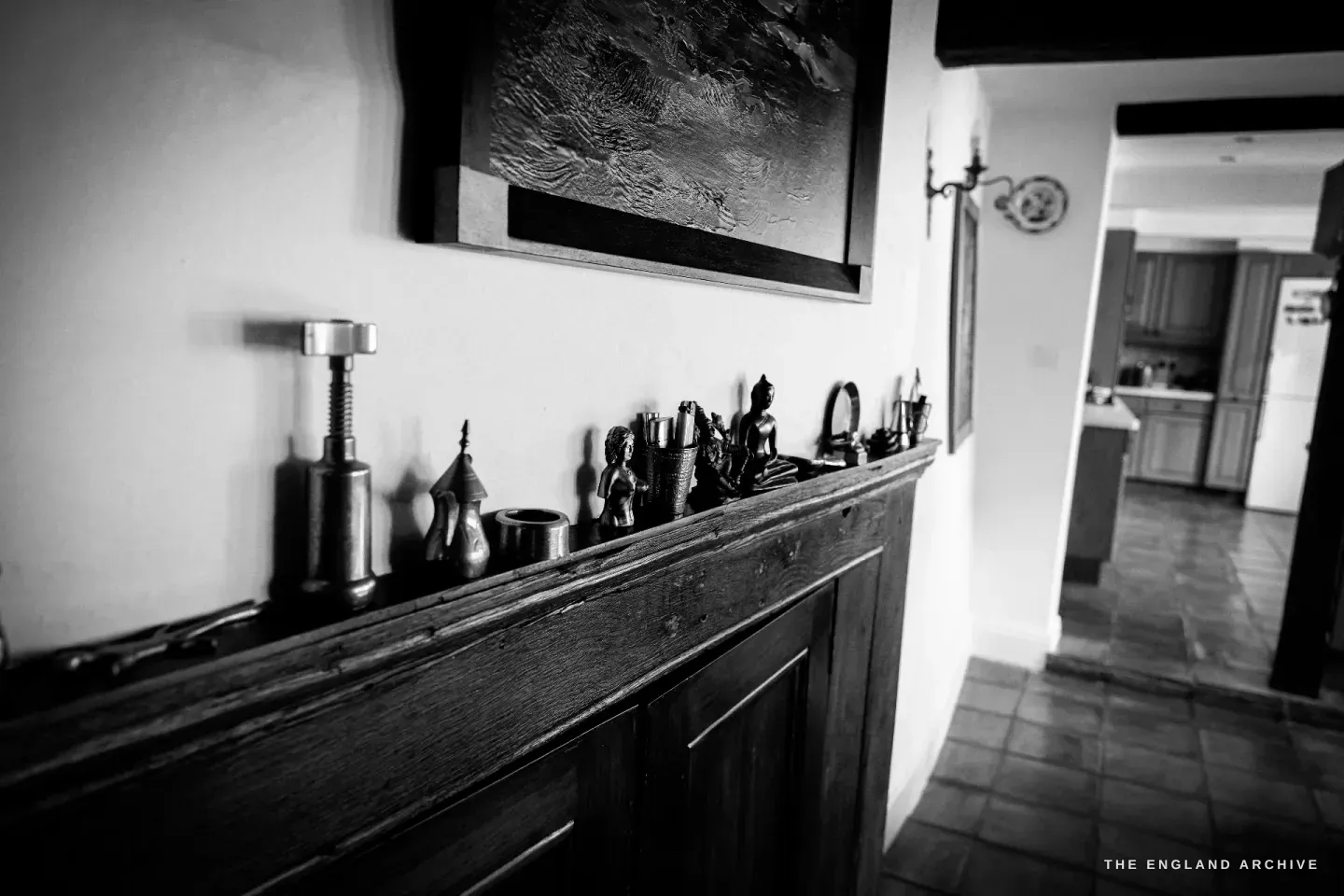 A dark oak ledge in Carol's hall set with small bronze figures and a cast-iron Robert Welch nutcracker, beneath a large abstract painting.