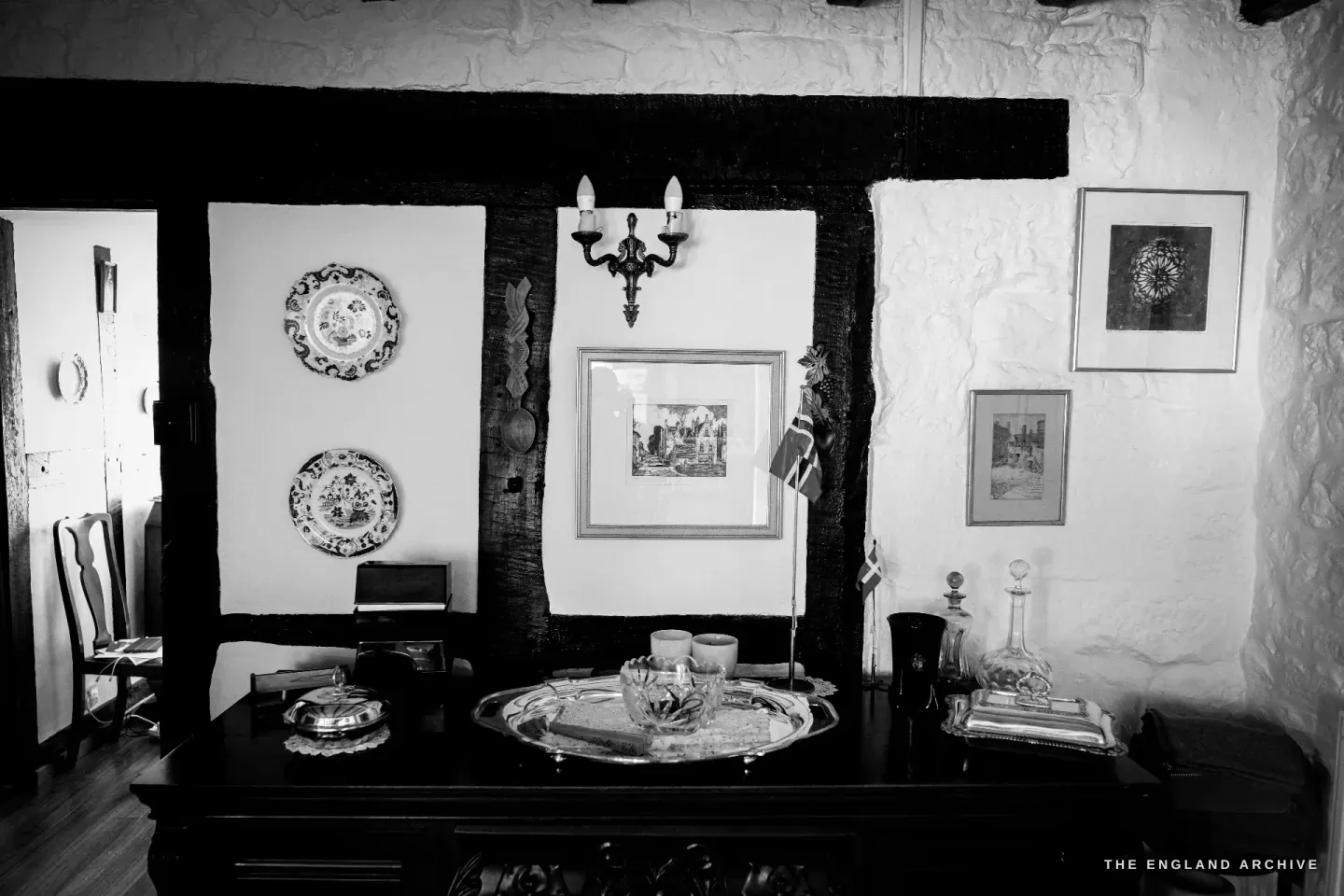 A wall of treasures in Carol's dining room - transferware plates, a brass candle sconce, framed prints and a small Danish flag above a silver-laid sideboard.