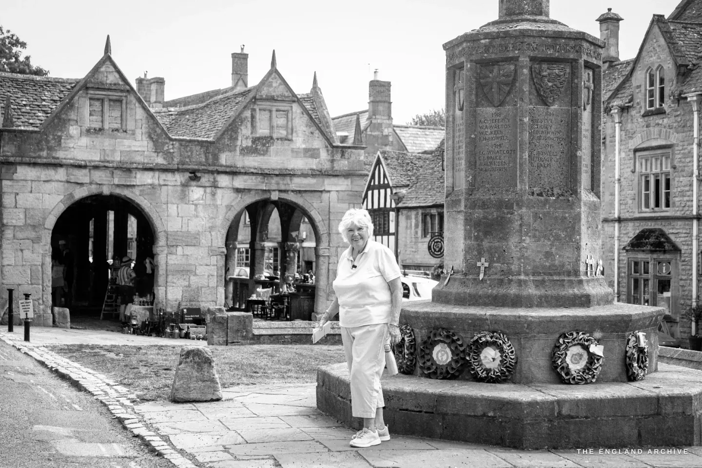 Carol beside the war memorial on the High Street, the open arches of the 1627 Market Hall behind her.