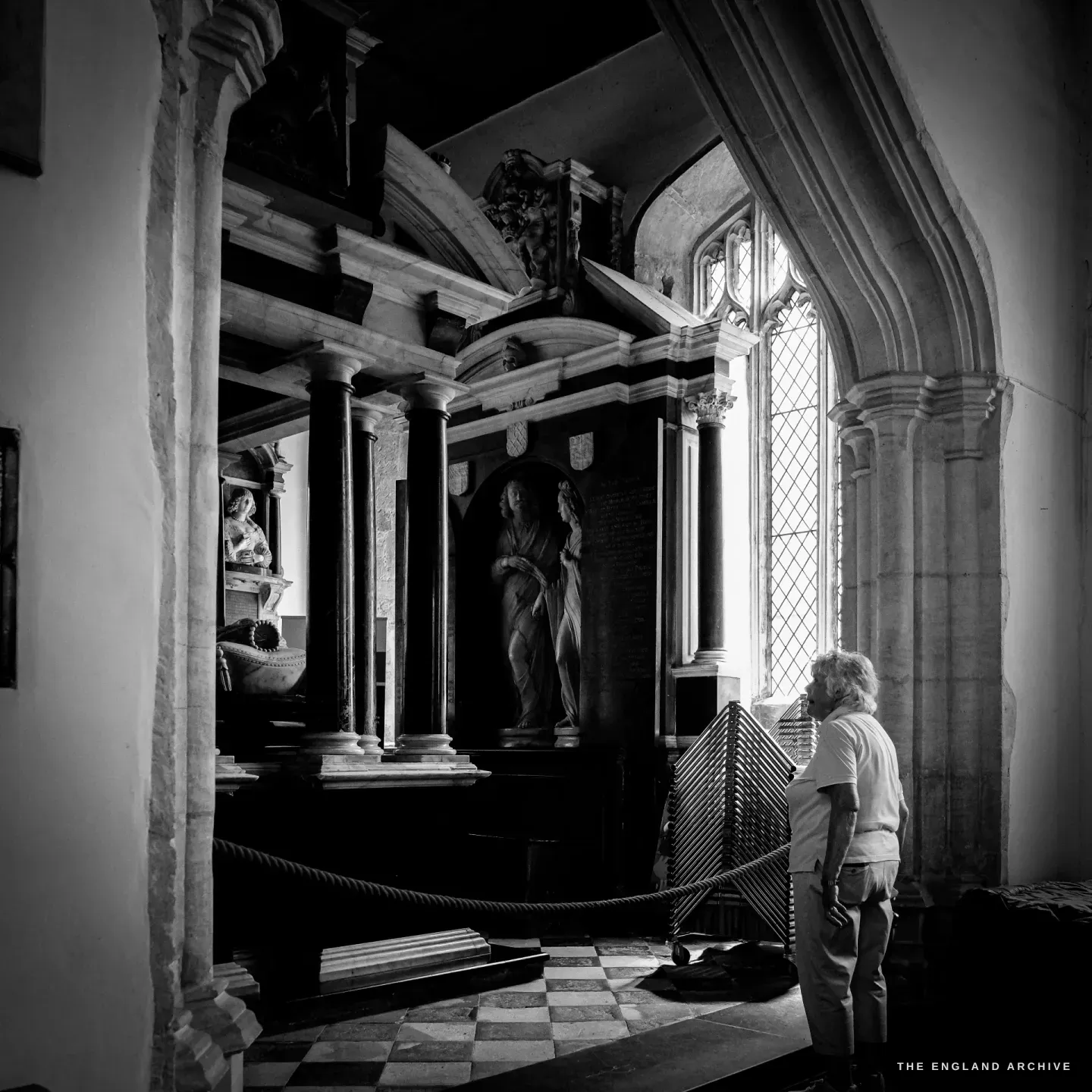 Carol standing small against a tall Gothic window in St James' Church, looking up at the canopied Hicks monument.