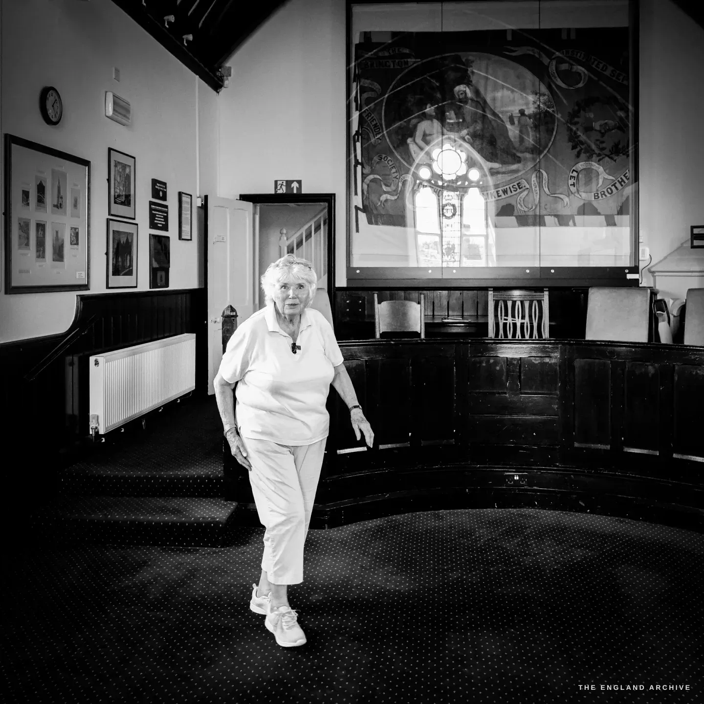 Carol on the curved wooden gallery of the Court Room of the old Police Station, beneath a large painted friendly-society banner.