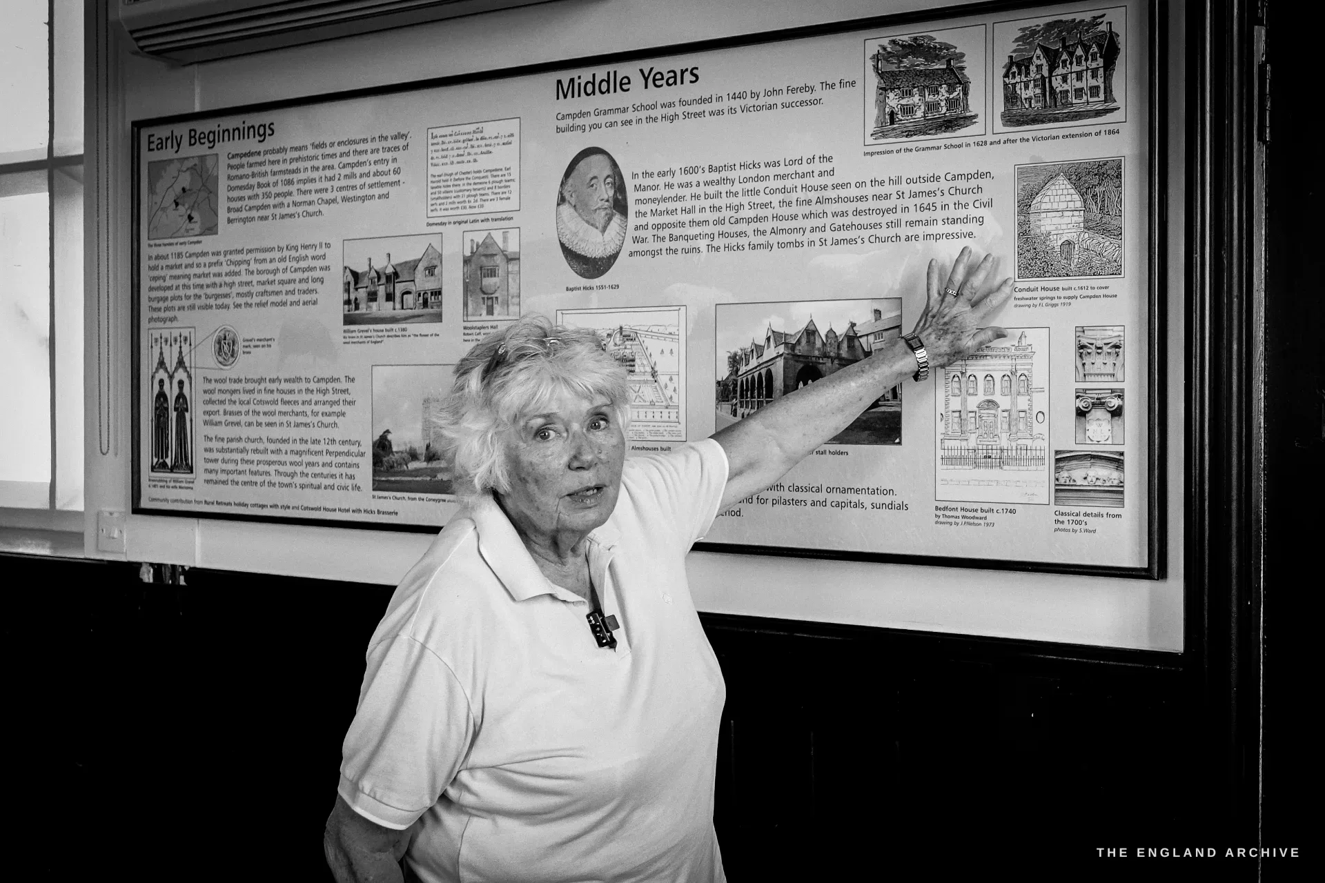 Carol with one arm raised, explaining the 'Early Beginnings' and 'Middle Years' history boards mid-sentence.