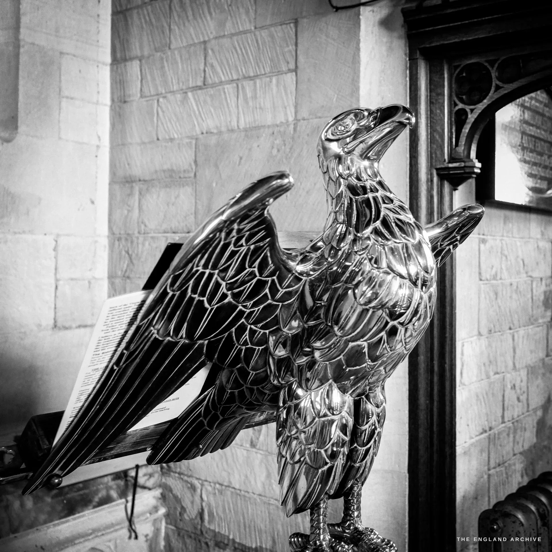 A polished brass eagle lectern with an open book on its outstretched wings, against a stone wall.