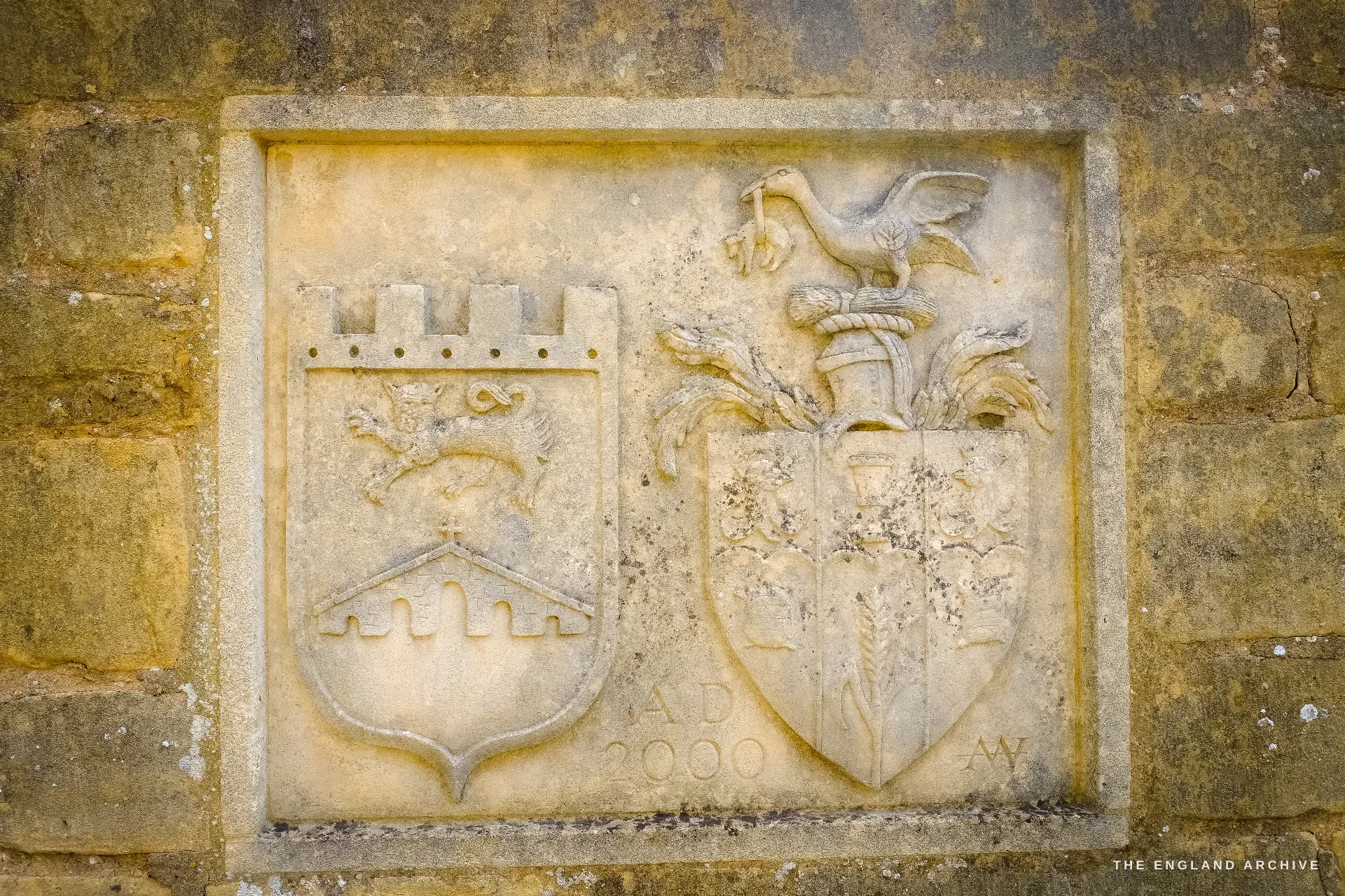Close on the two carved stone heraldic shields set in the wall, one castellated with a rampant beast, the other crested with a bird, dated AD 2000.