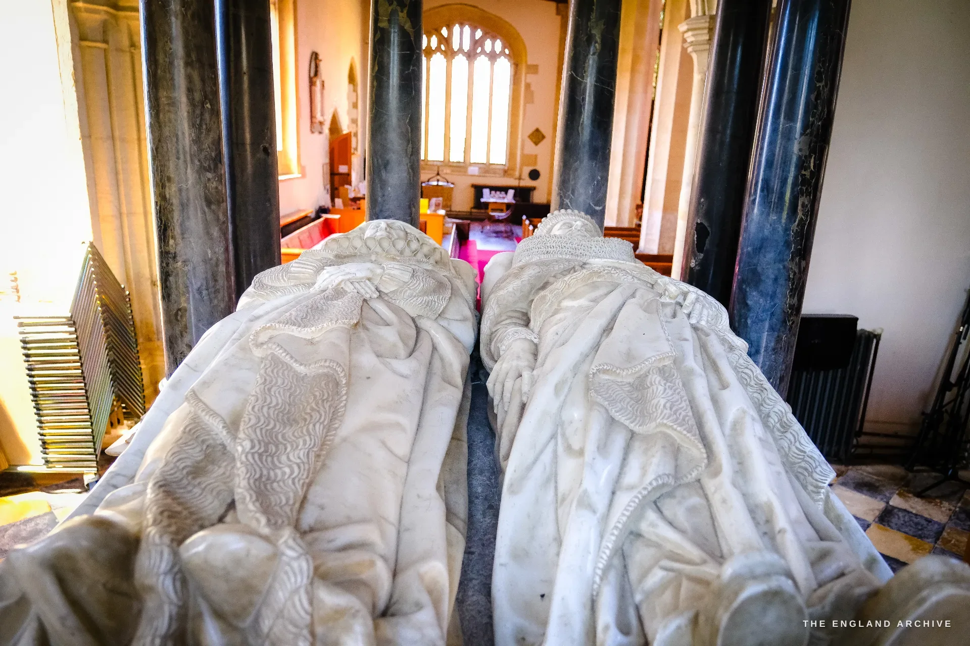 Close on the two recumbent marble effigies of Sir Baptist Hicks and his wife Lady Elizabeth under the tomb canopy, coronets on their heads and hands at rest between black marble columns.