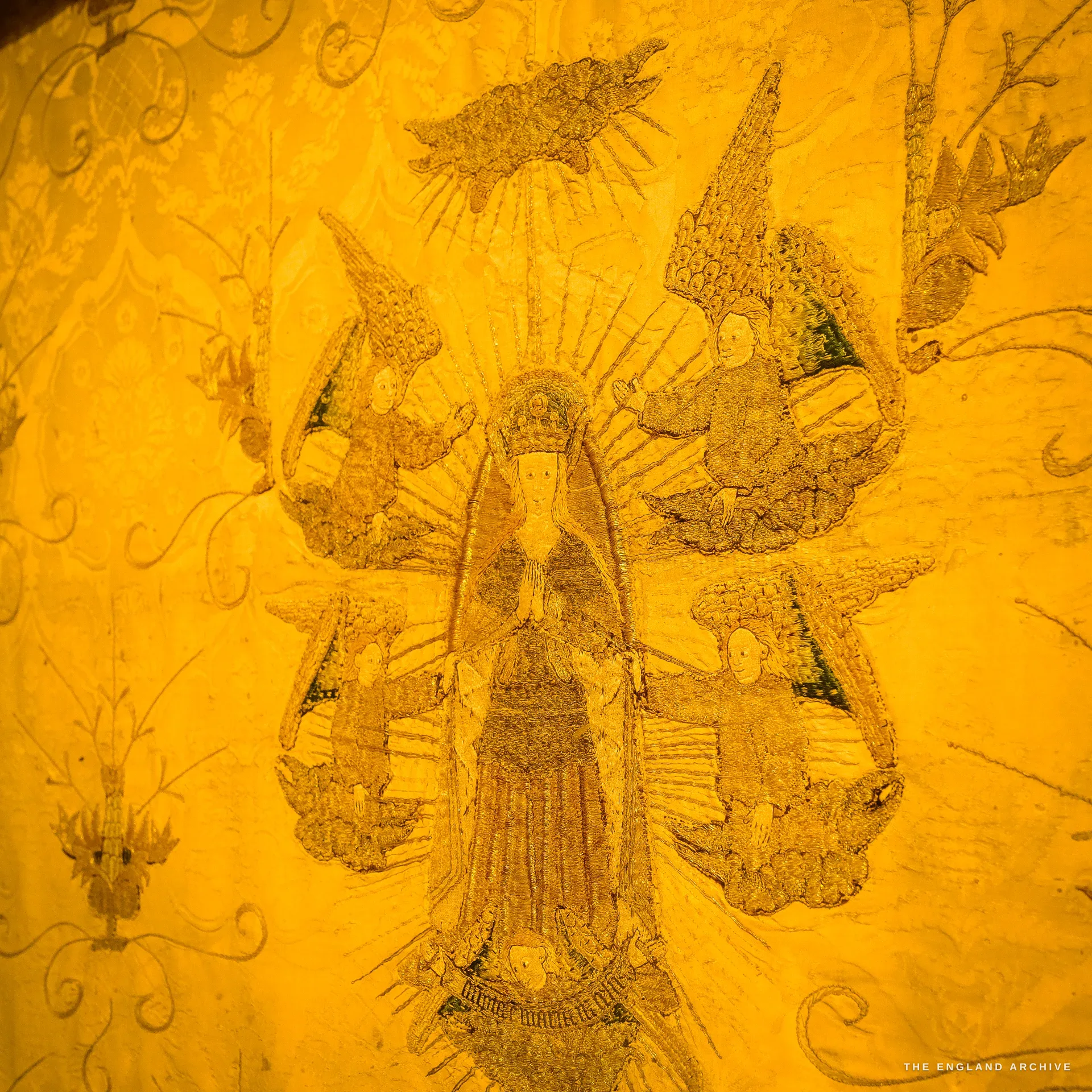 Close on the gold-worked embroidery of one of the medieval Campden altar cloths, figures on aged fabric, lit warm.