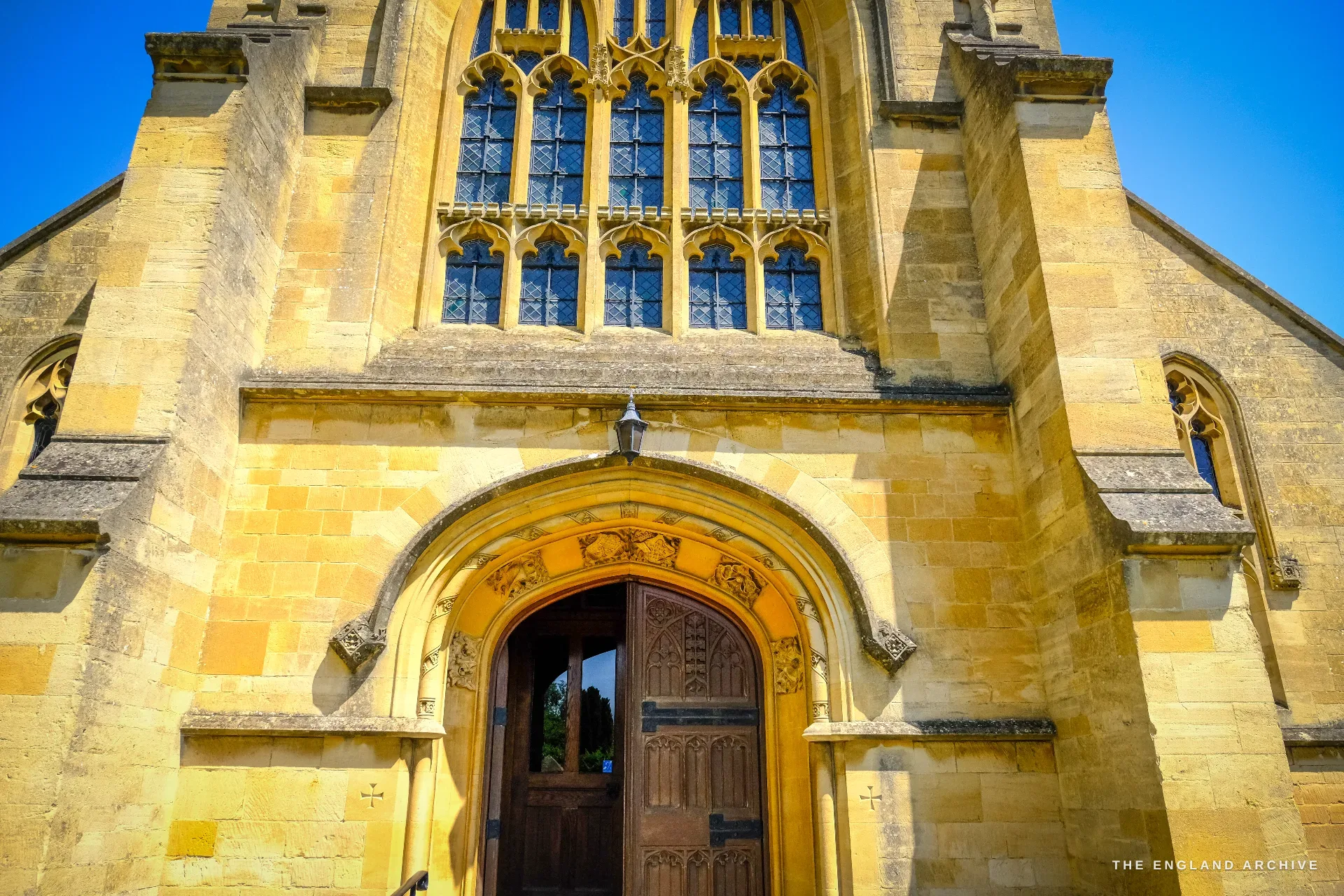 The west front of St Catharine's Catholic Church, a tall traceried window over an open arched oak doorway between pinnacled buttresses.
