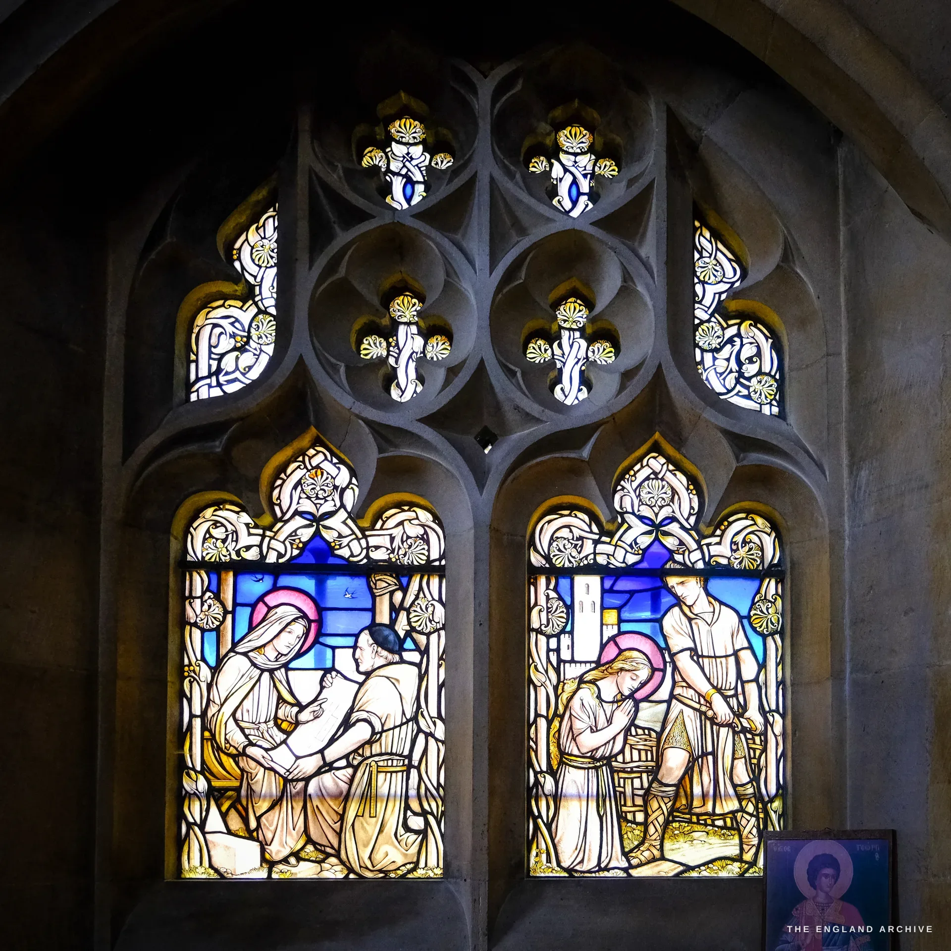 A two-light stained-glass window of haloed female figures in genre and parable scenes, with ornate cusped tracery above.