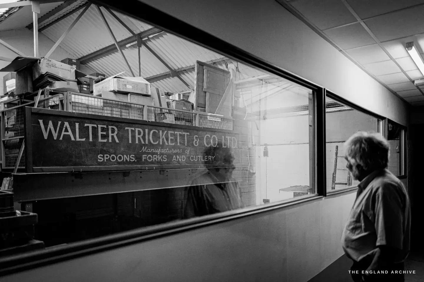 Chris Hudson at right looking through a glazed partition at the old Walter Trickett & Co sign mounted on the far wall.