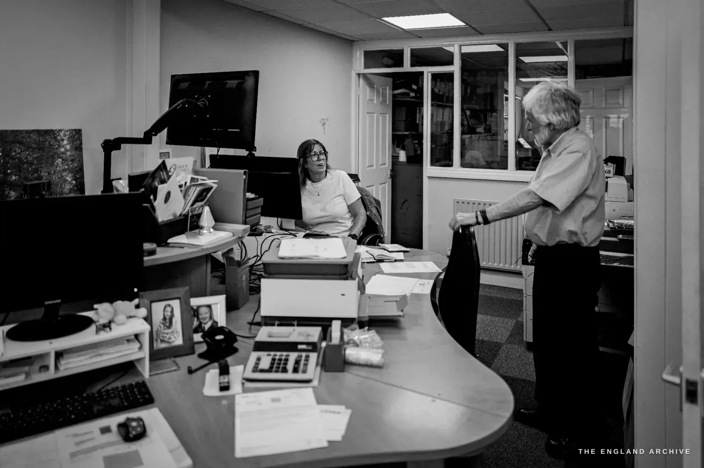 The Chimo office: Karen seated at her desk and computer at left, Chris standing across the desk from her at right.