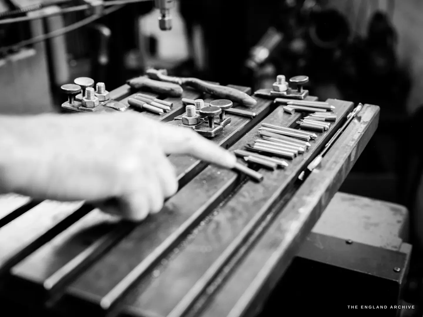 Chris’s hand resting beside rows of slim steel hand punches laid in a rack on the bench.