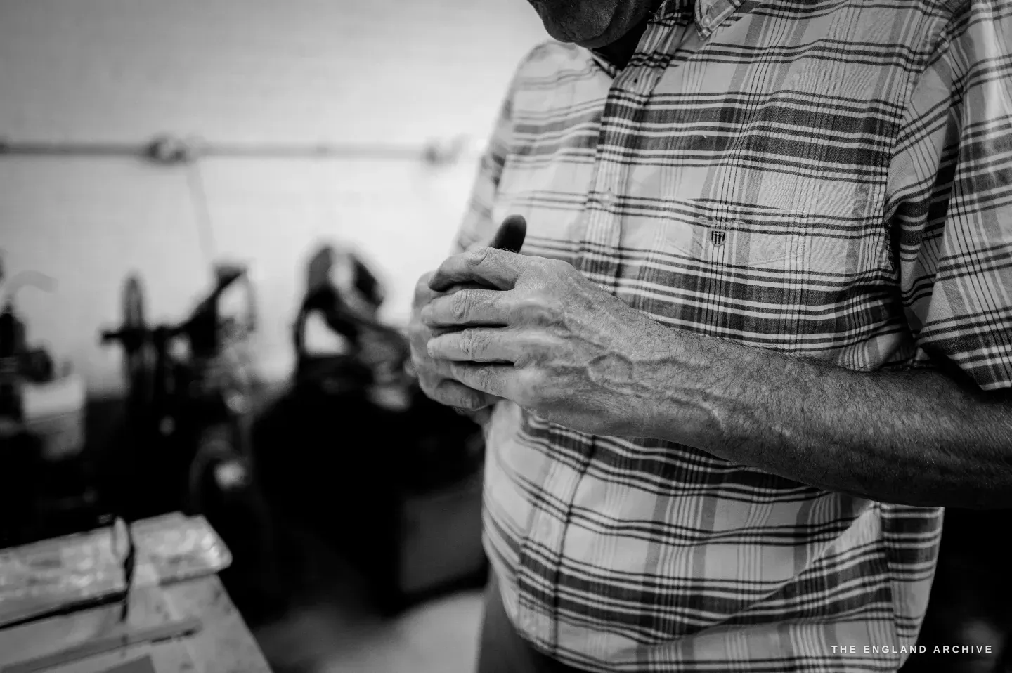 Chris standing with his hands held together at his chest, mid-explanation, engraving machines blurred behind him.