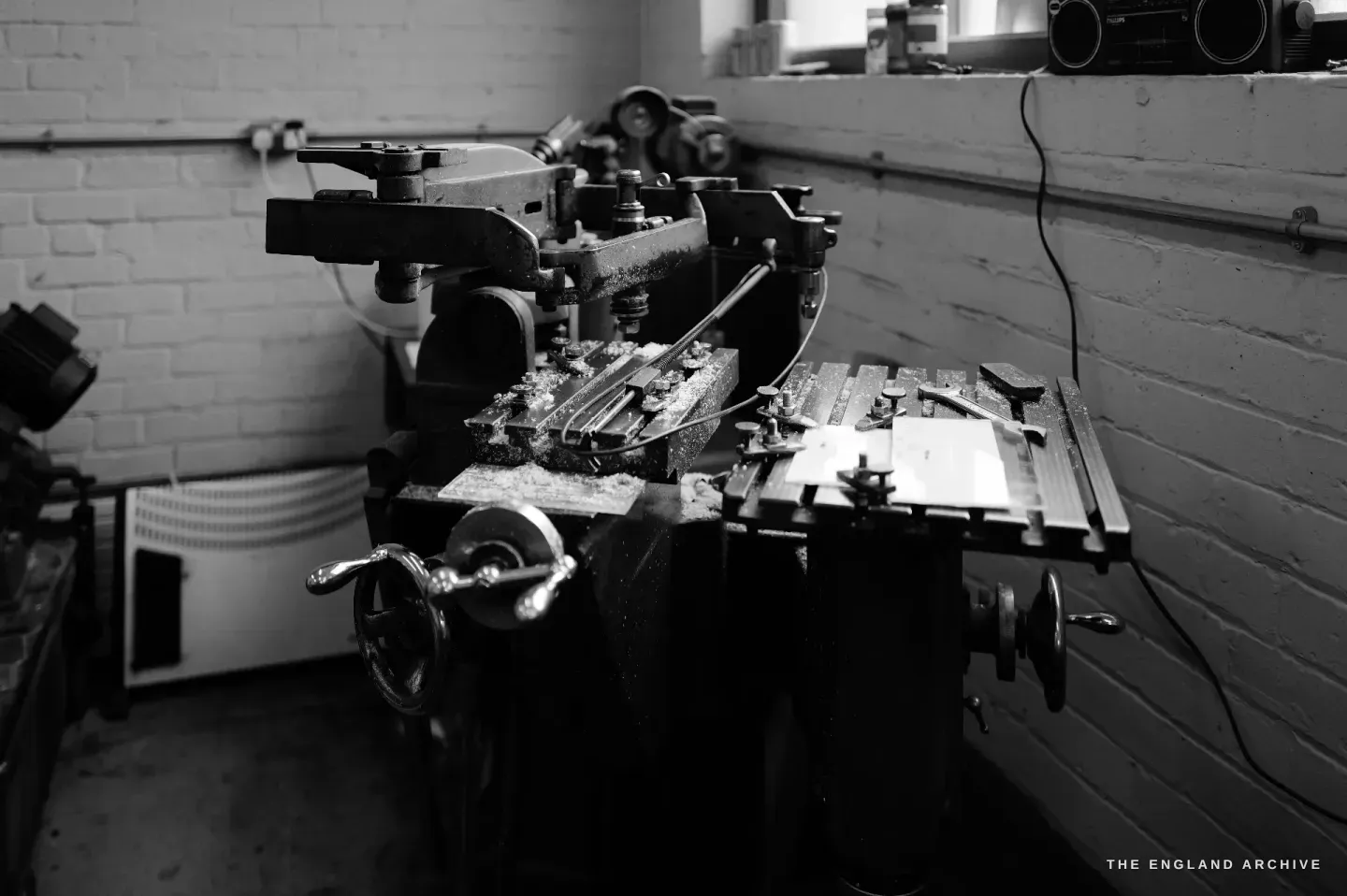 A side view of a heavy pantograph die-sinking machine, its geared arm and sliding bed reaching across the bench.
