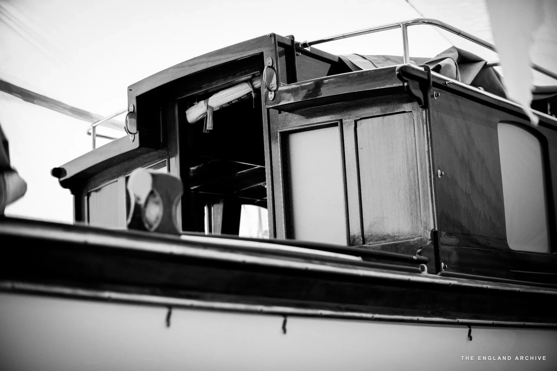A close view of the cabin and rear deck of a wooden river launch, varnished surfaces and brass detail in the workshop light.