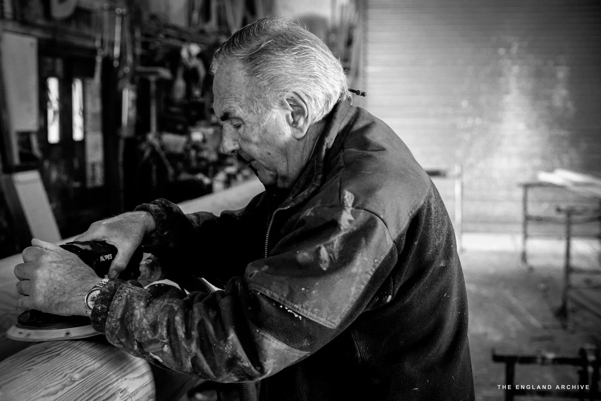 A sharp digital frame of Michael Dennett in profile, sanding a piece of timber at the bench, every detail held.