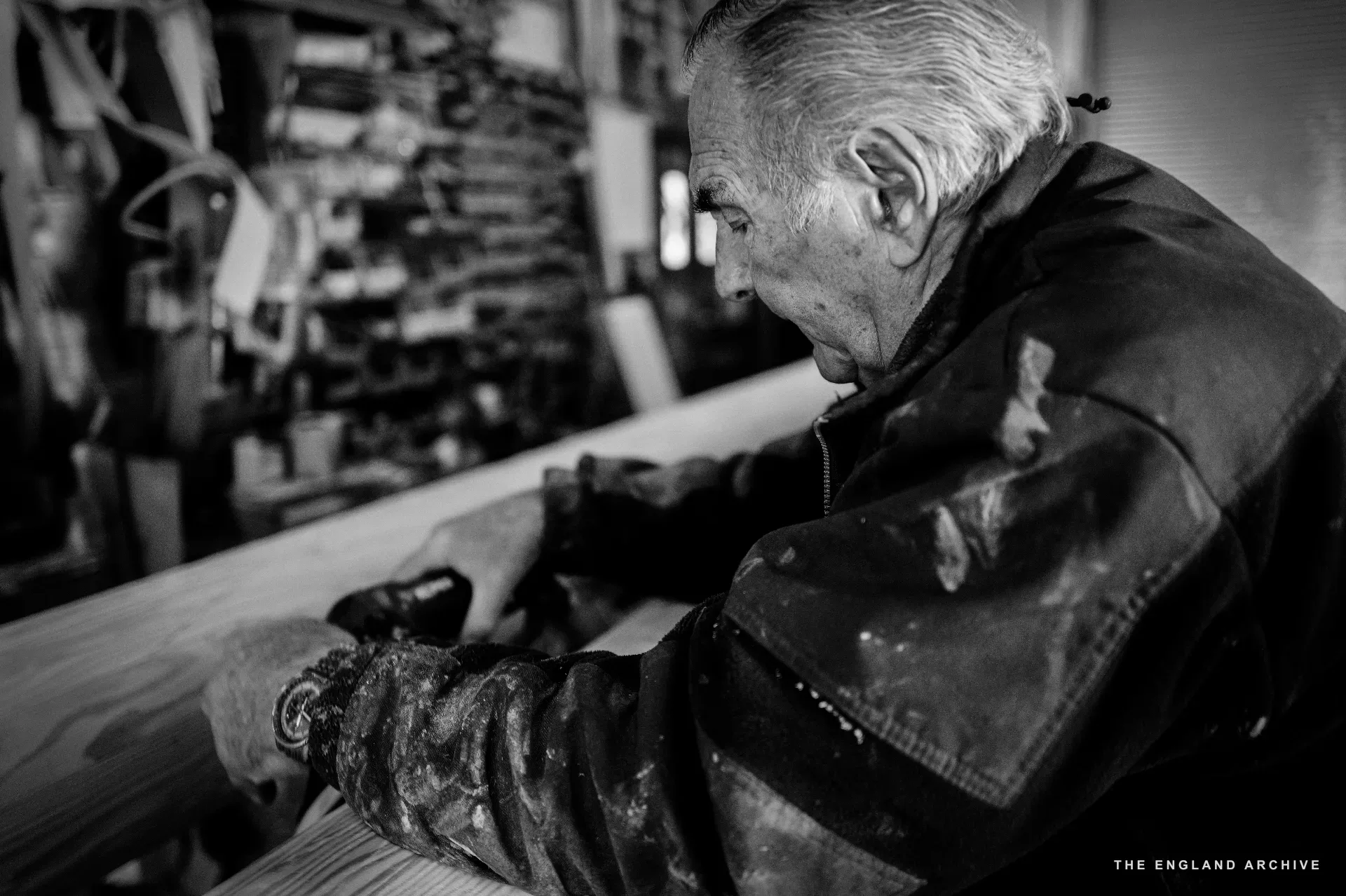 A close on Michael Dennett’s hands sanding a length of timber at the bench, the side of his jacket and the timber surface filling the frame.