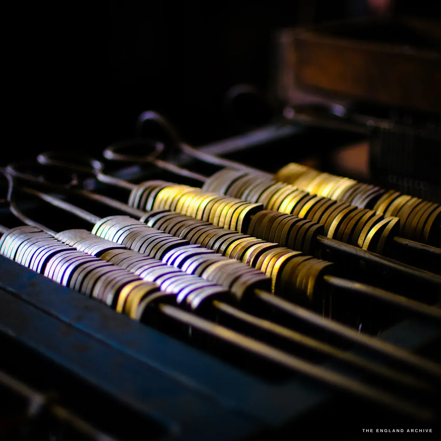Rows of part-finished scissor blades racked on steel rods, their ground edges catching bands of light, in the dark of the workshop.
