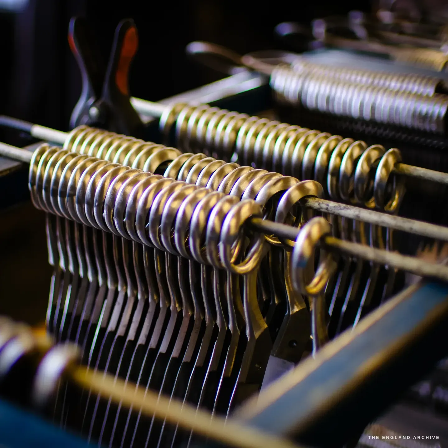 Rows of part-finished scissor bows threaded close together on steel rods, catching the light, a spring clamp behind.