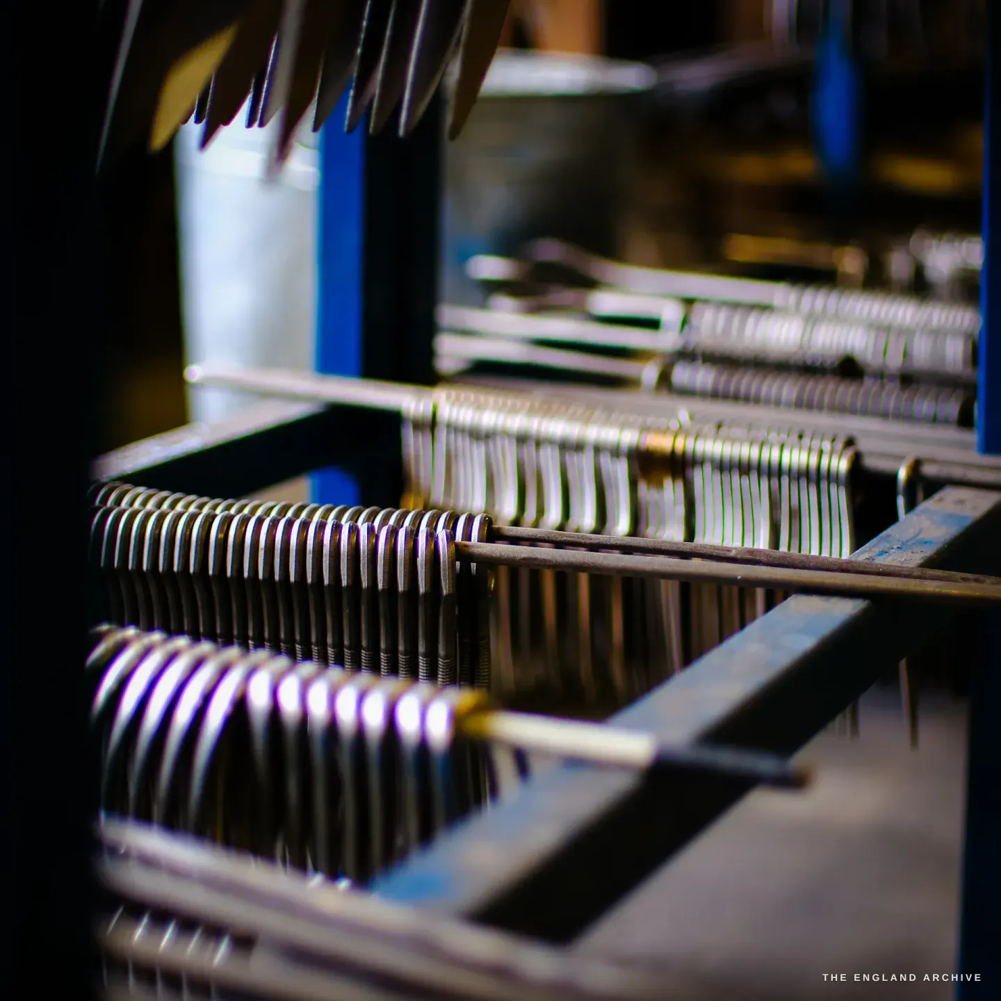 Part-finished scissor halves threaded in dense rows on steel rods along a bench.