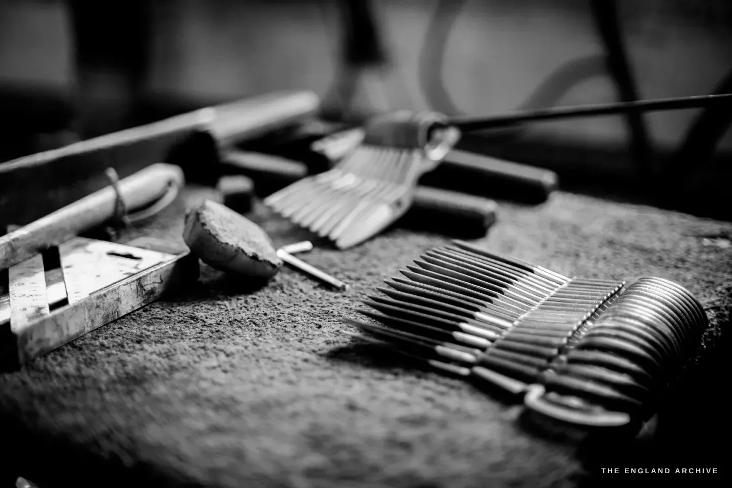 A bench scattered with small embroidery blades and bows alongside hand tools - pliers, a leather pad, a fine rule.