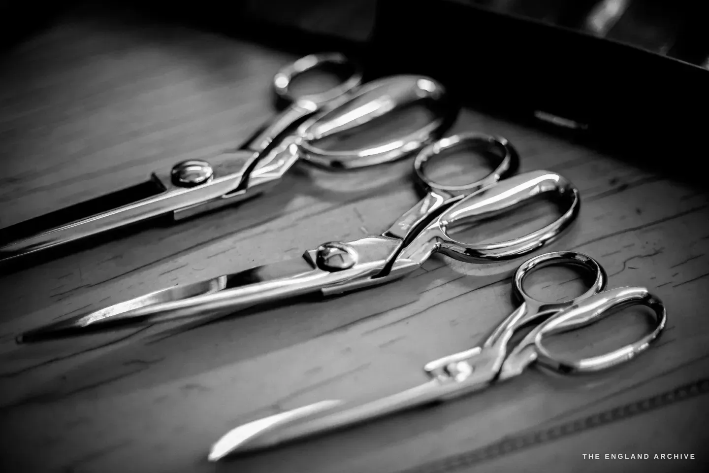 Three finished scissors laid in a row on a wooden surface - a tailor’s shear, a household scissor and a smaller general pair.
