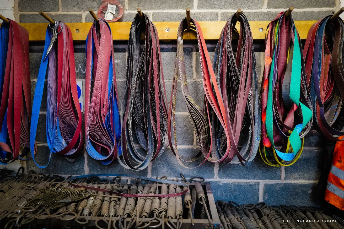 Loops of abrasive grinding belts of different grades hung in rows along a wall, coiled springs and parts in a tray below.