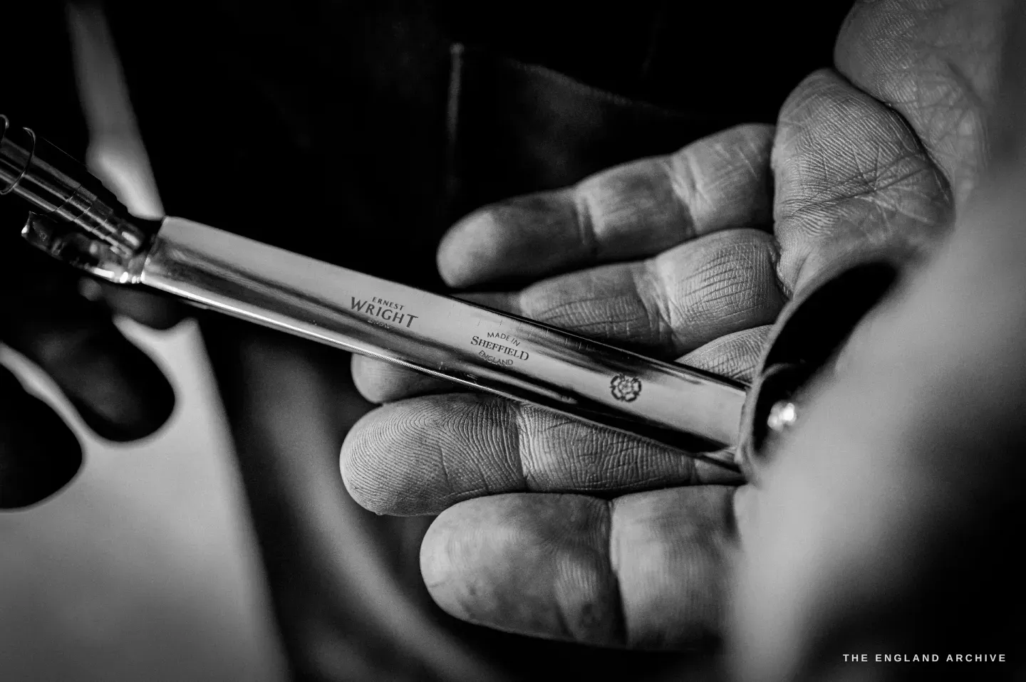 A finished scissor blade held across a hand, the ERNEST WRIGHT maker’s mark and SHEFFIELD etched along the steel.