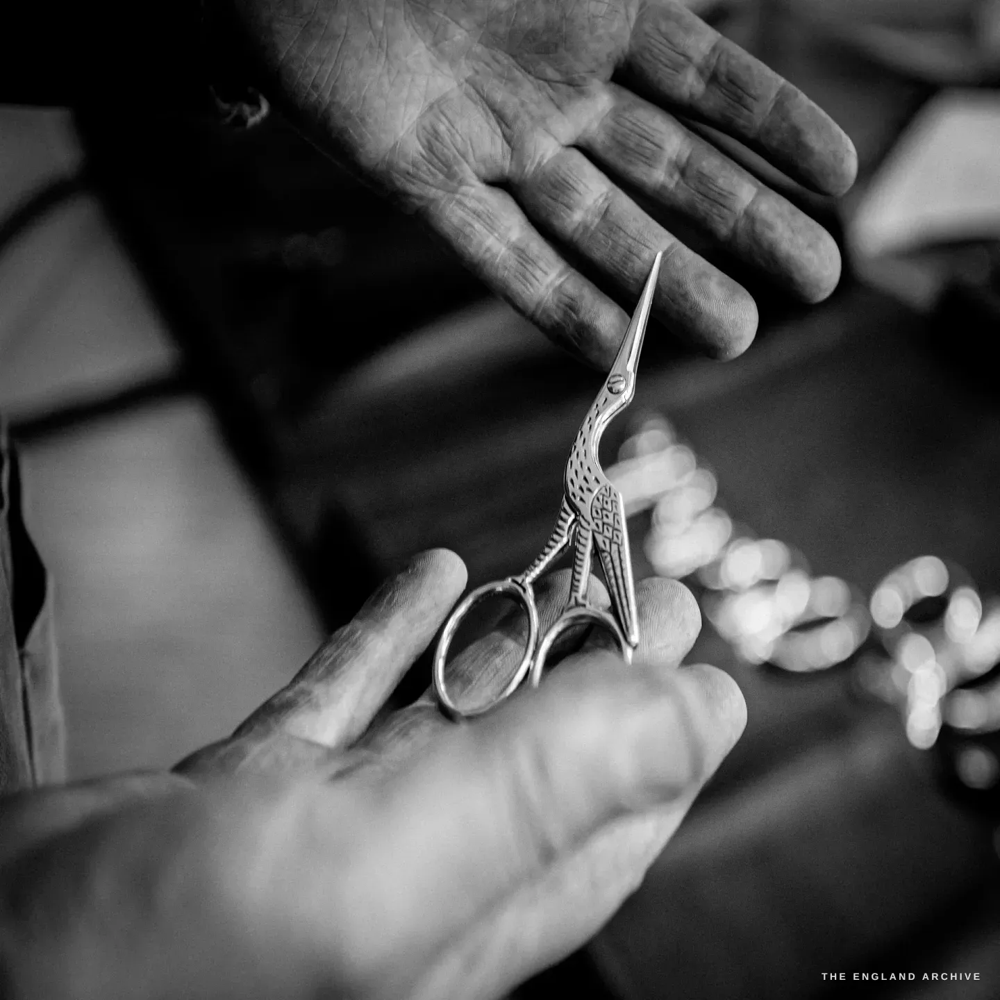 A maker holds a pair of stork embroidery scissors between his fingertips, the slim curved blades forming the bird's beak.