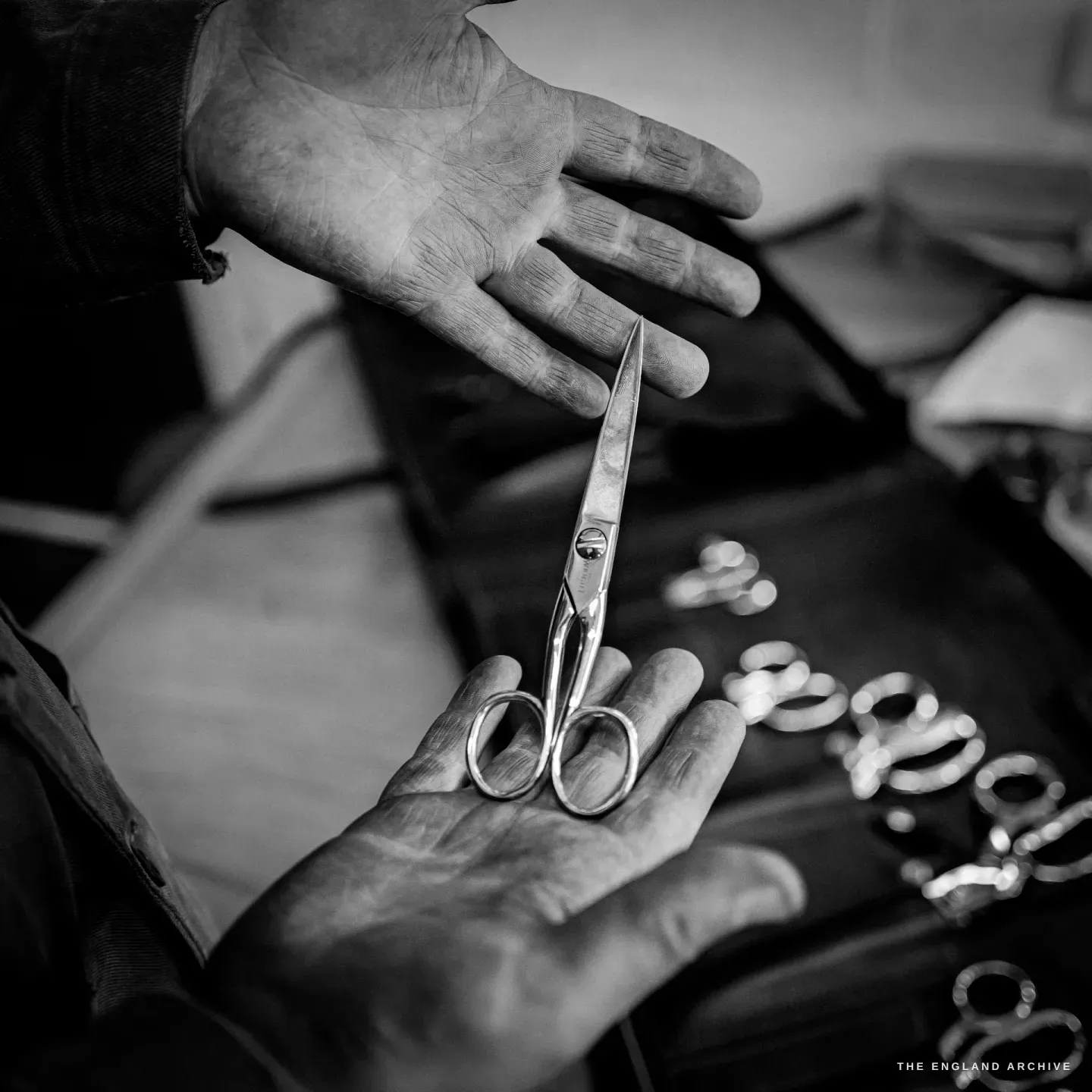 A pair of long slim-bladed trimming scissors with small round bows held up in a maker's hand.