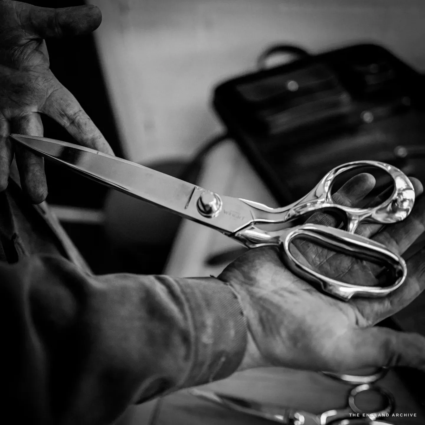 A pair of long side-bent tailor's trimming scissors held up in a maker's hand, the blade etched WRIGHT.
