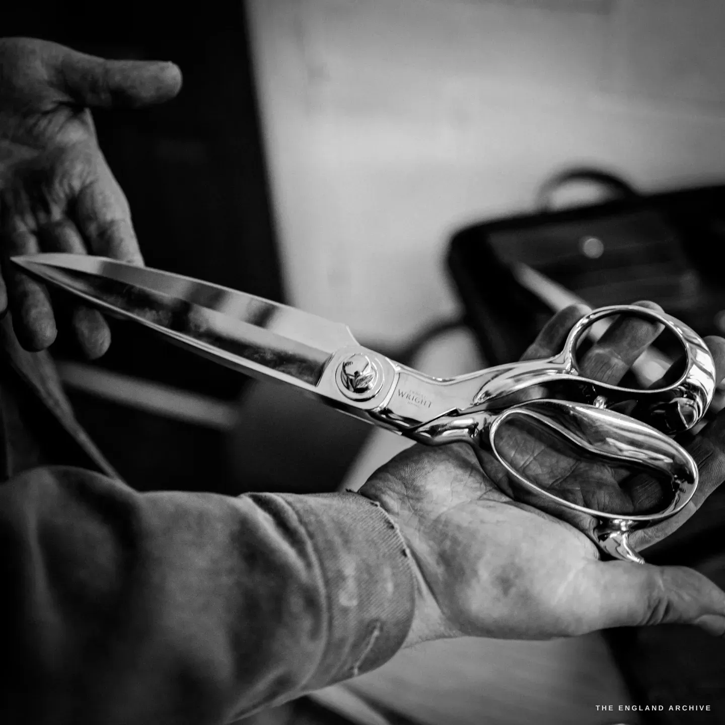 A large pair of side-bent tailor's shears held across a maker's hands, mirror-polished, etched ERNEST WRIGHT.