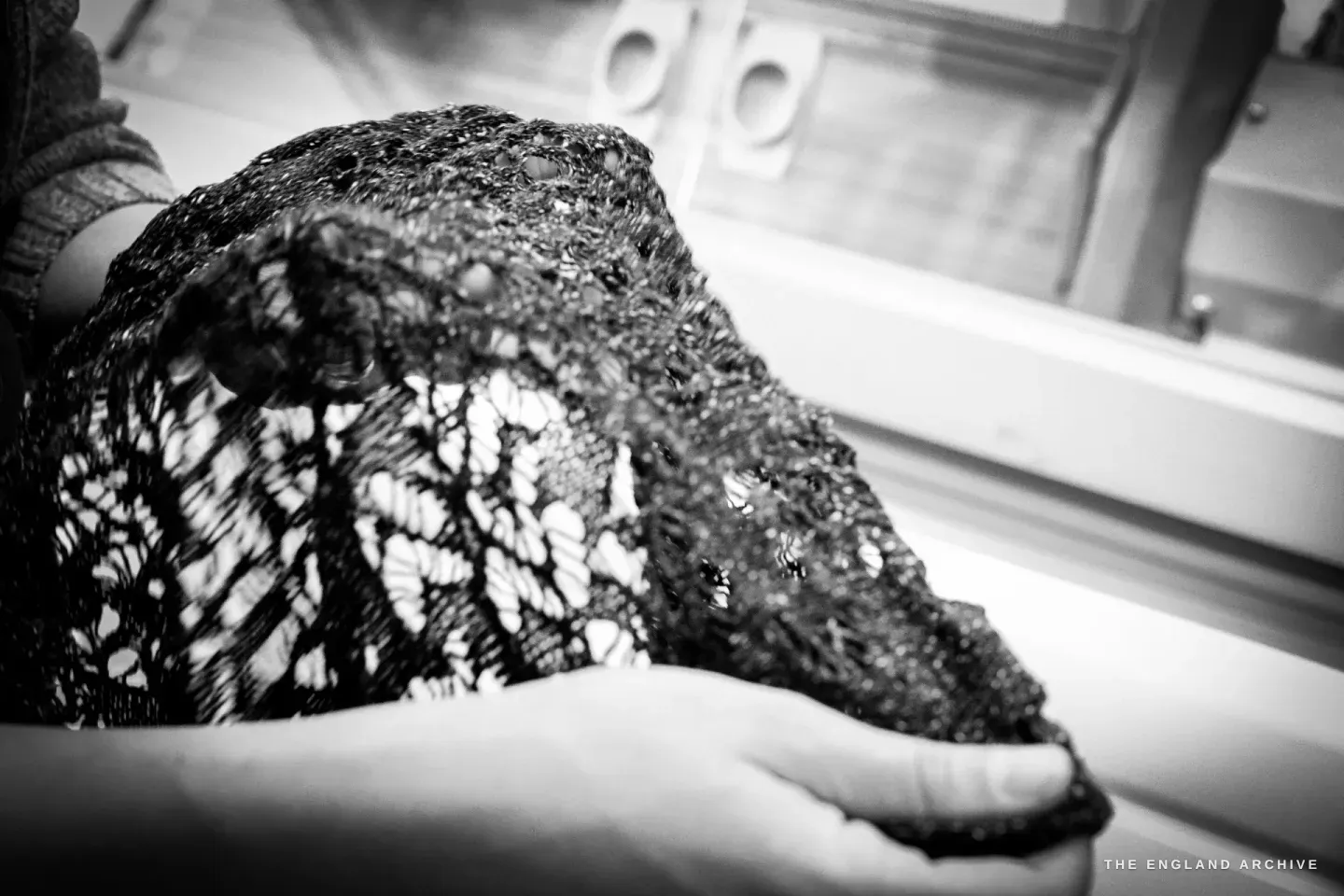 Hands holding an openwork lace-knit panel up to the light, the stitch structure showing through.