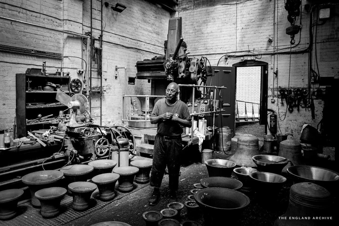 Giridhar standing among ranks of small bells and the tuning machines, holding a small tool, explaining the work.