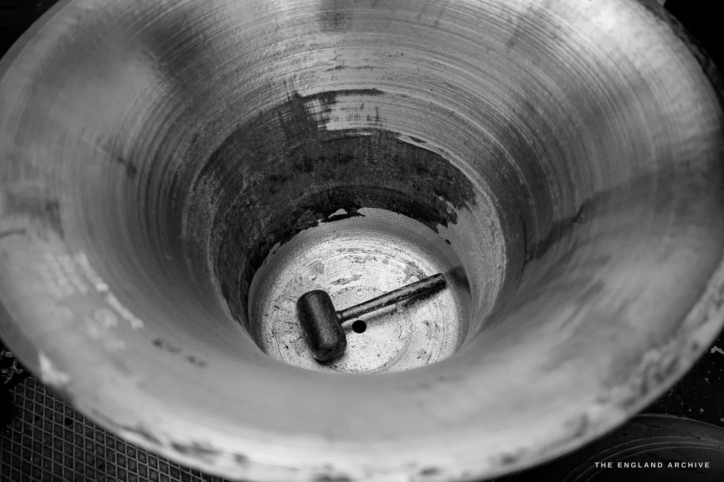 Looking straight down into the inside of a bell on the tuning machine, a steel cutting tool clamped across its throat where it bites the metal.