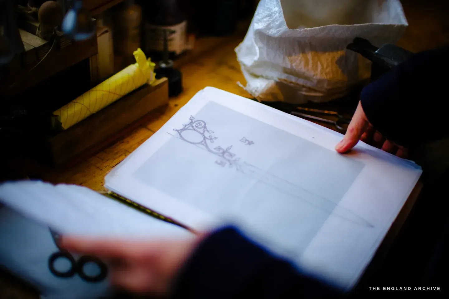 Grace Horne&rsquo;s hands over a sheet of translucent paper carrying a fine, ornate scissor design of looping stems and flowers, tools and a taped roll behind.
