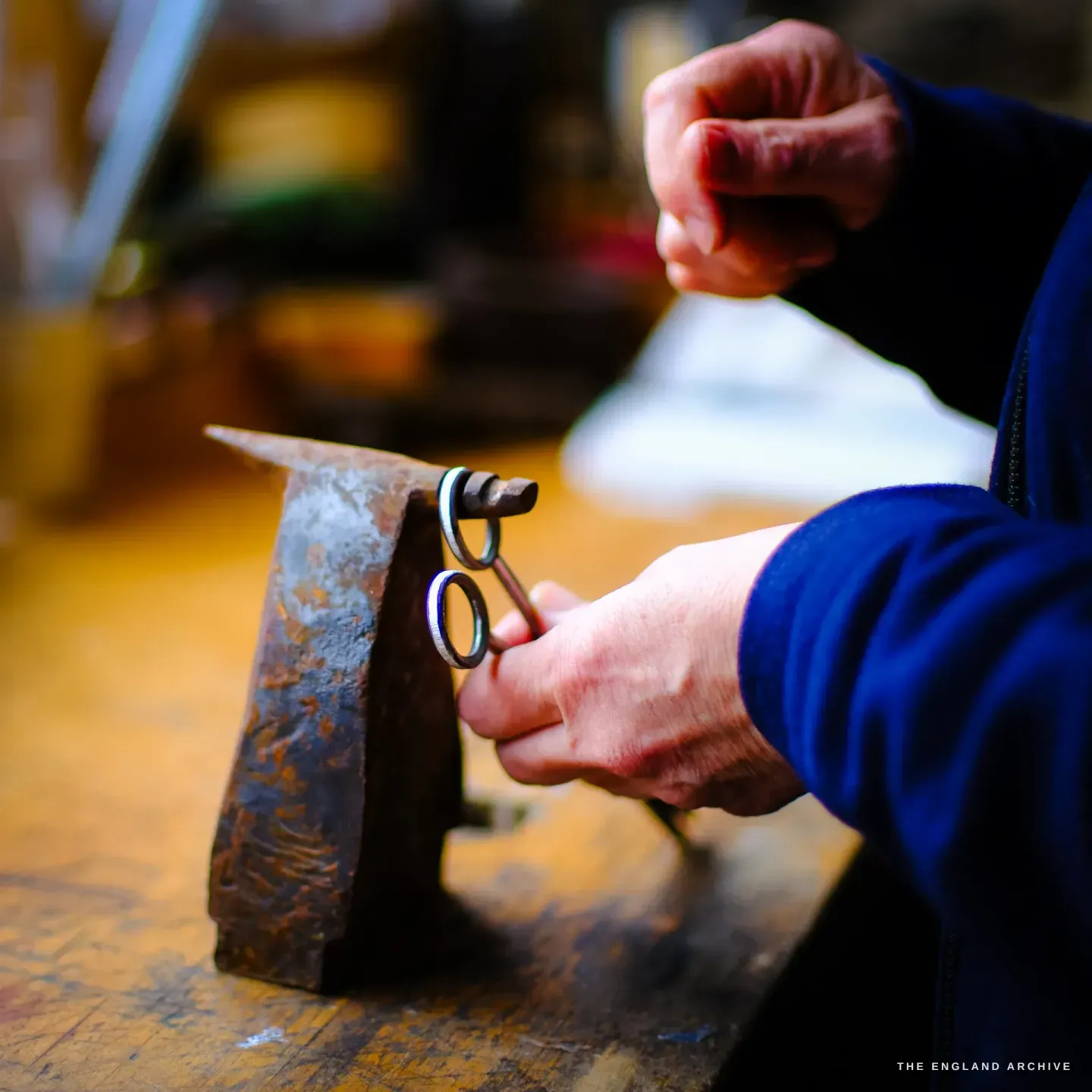 Grace Horne&rsquo;s hands work a small pair of forged scissors against a rusted beak anvil at the bench, in warm light.