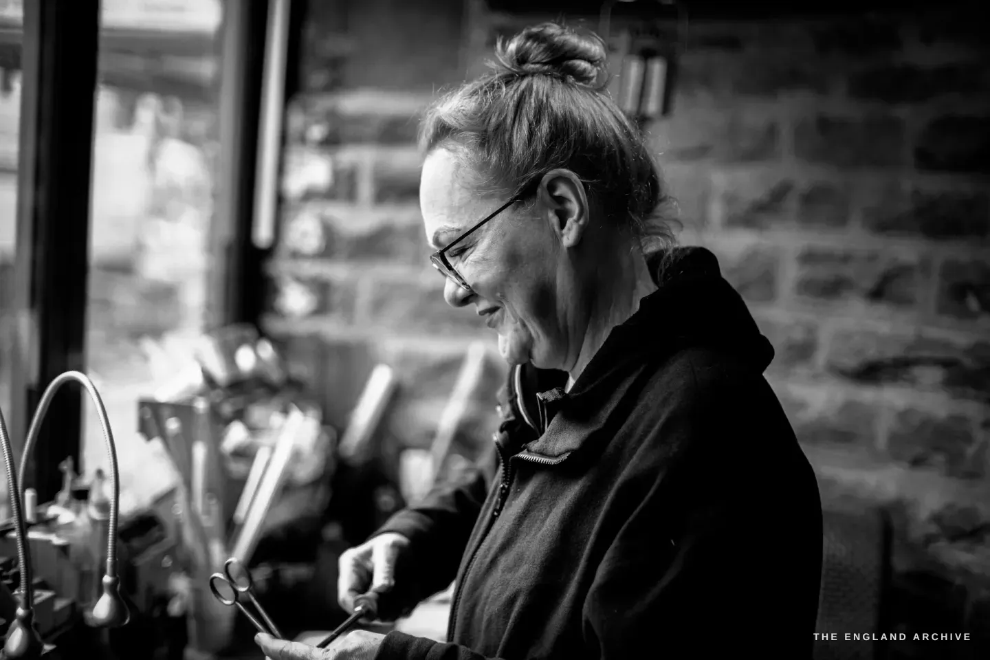 Grace Horne stands at her bench by the window, smiling down at a small pair of scissors in her hands.