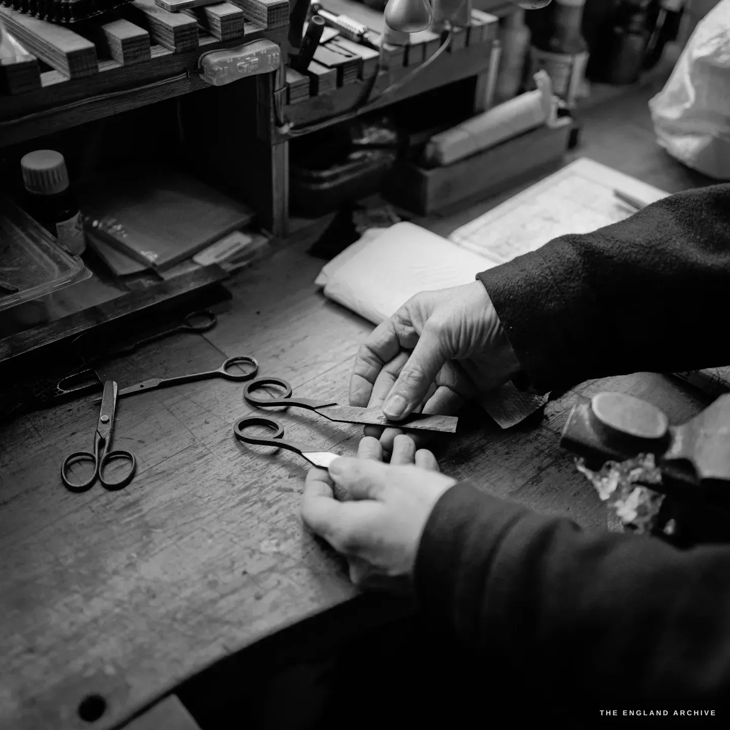 Grace Horne&rsquo;s hands fit a small part to a pair of scissors at the bench, a finished pair and a forged blank resting on the wood.