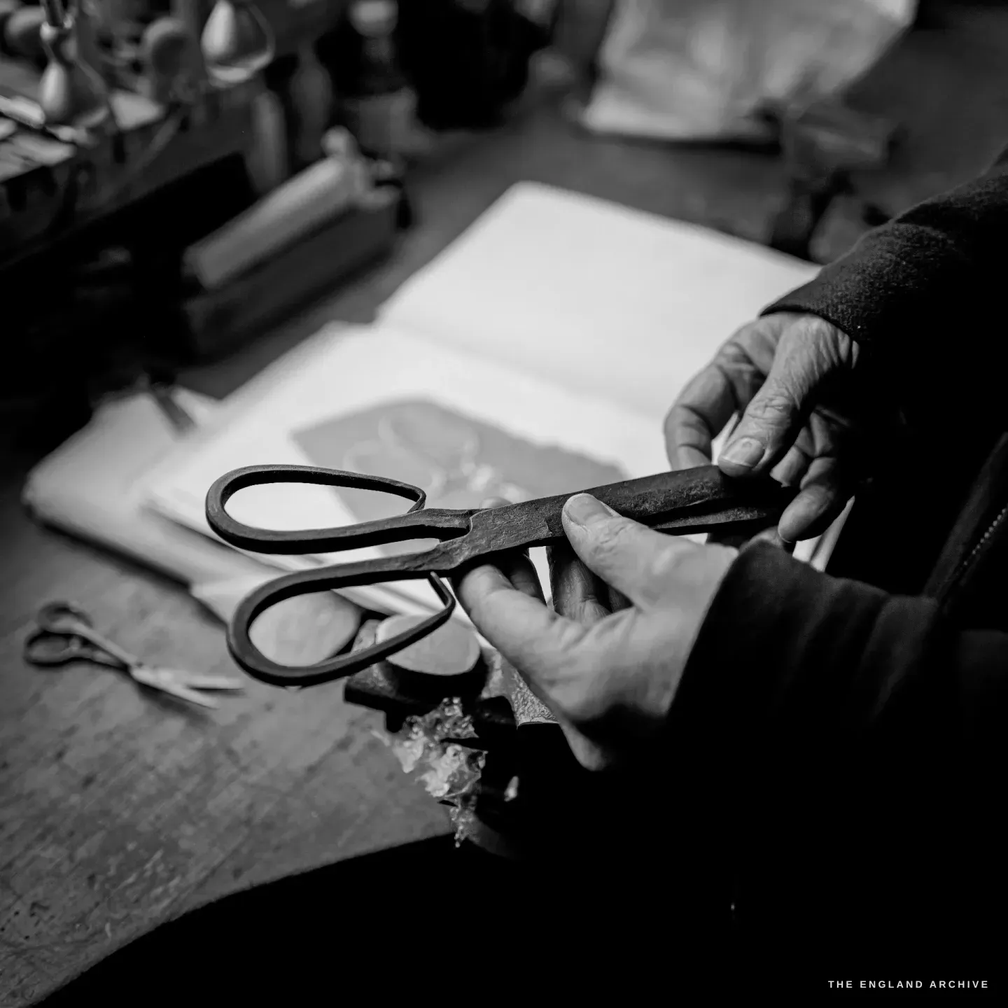 Grace Horne&rsquo;s hands hold a pair of hand-forged scissors with looped bows over an open book of scissor drawings.
