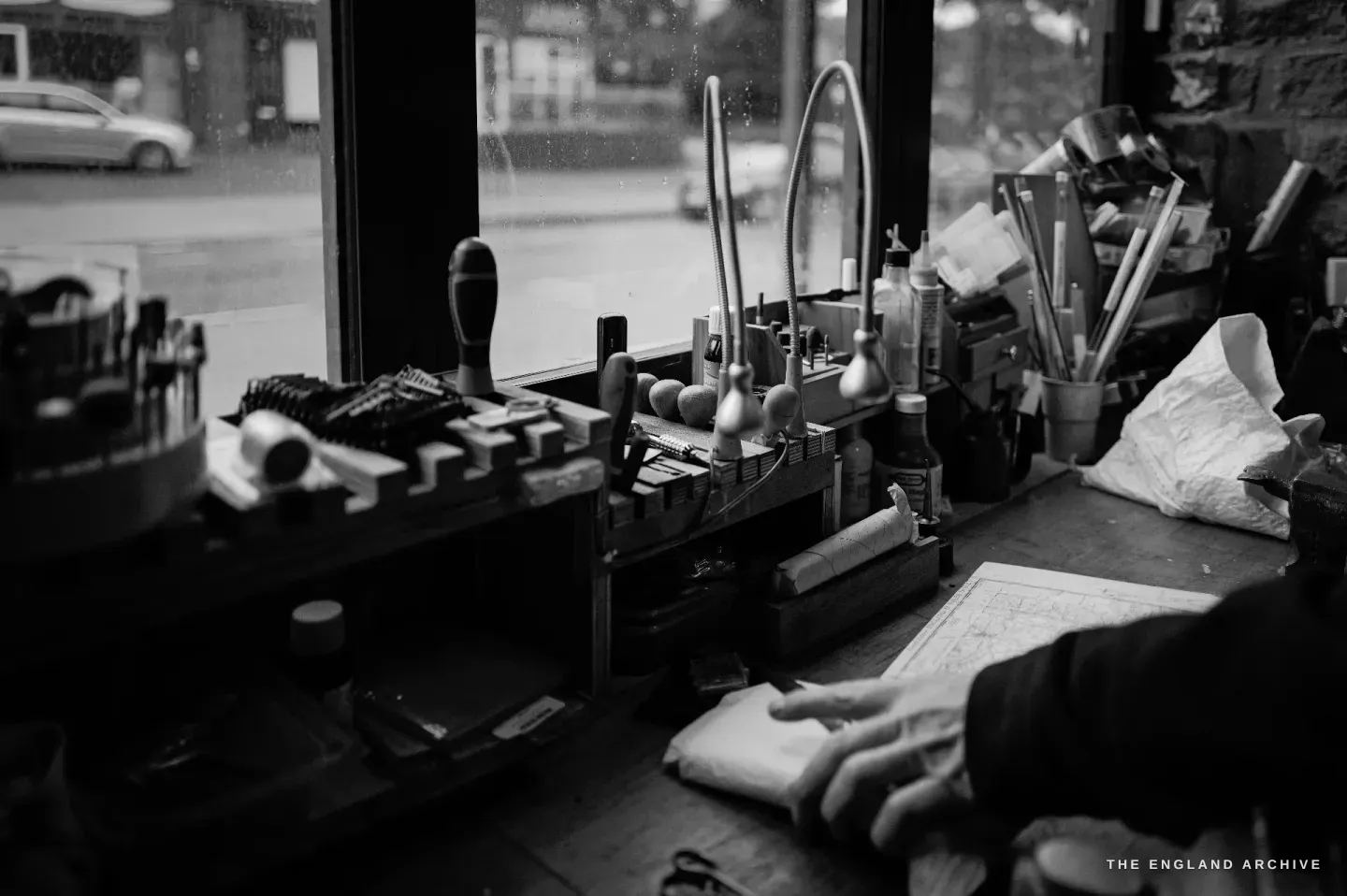 The workshop window looks out onto the street - a parked car and terraced houses - with the sill lined with hand tools in racks.