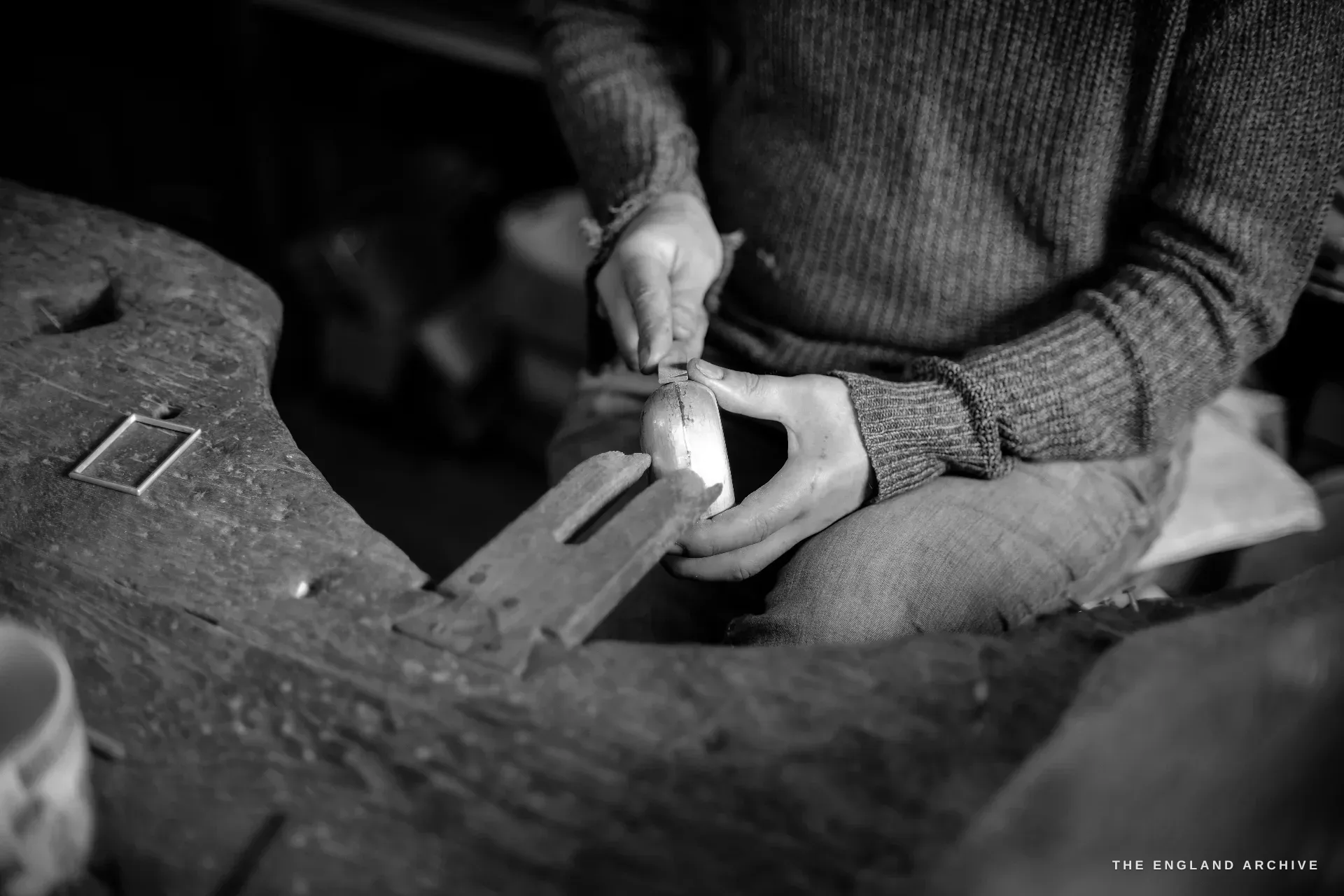 Seen from above, a craftsman's hands cradle a domed silver bowl on a wooden stake, working its edge with a small tool.