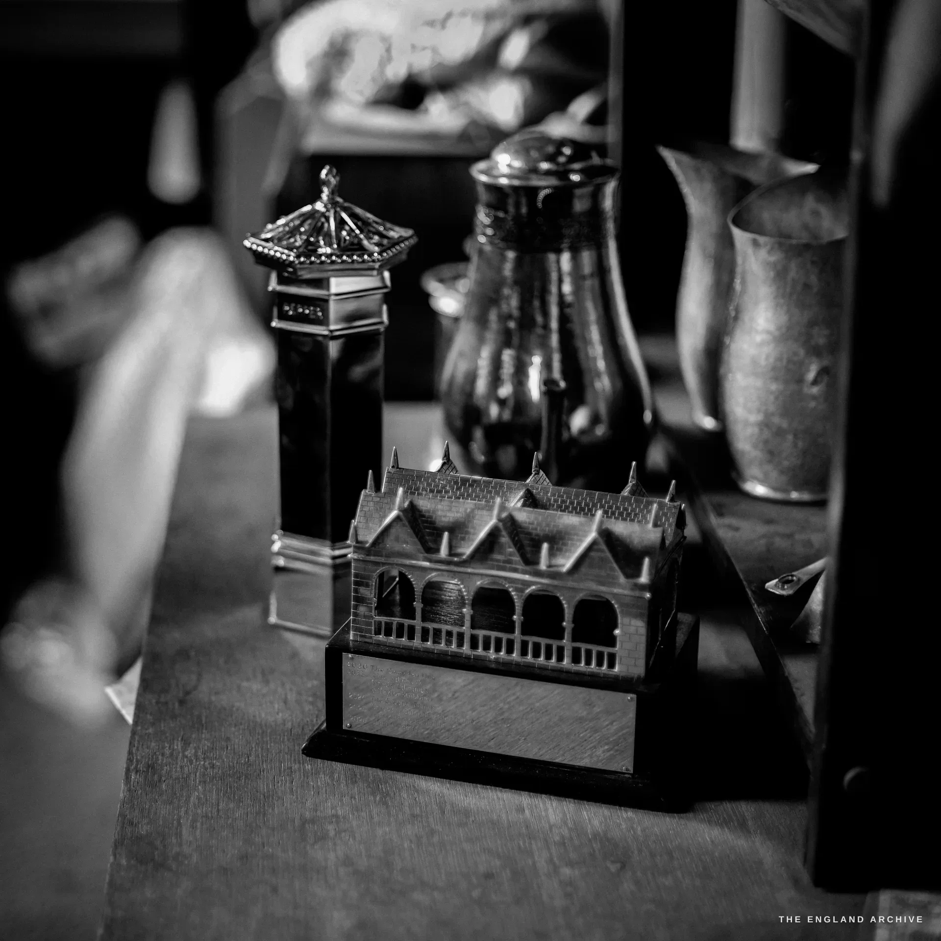 A silver model of the Chipping Campden Market Hall, its gabled roof and arched bays rendered in miniature, beside a tall caster and a glass condiment bottle.