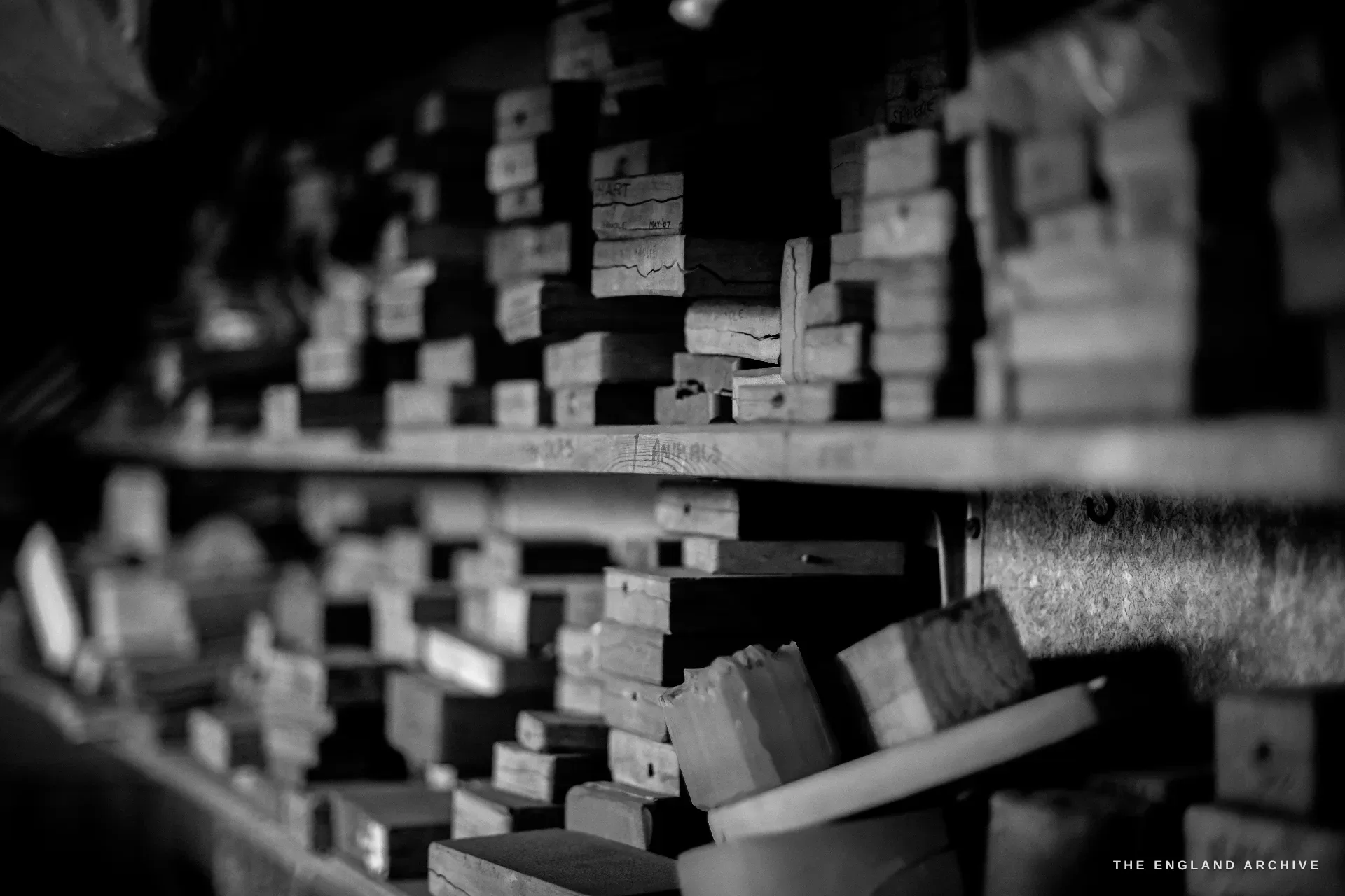 Deep shelves crammed with stored wooden pattern dies and stamping blocks, several pencil-labelled with job and date references.