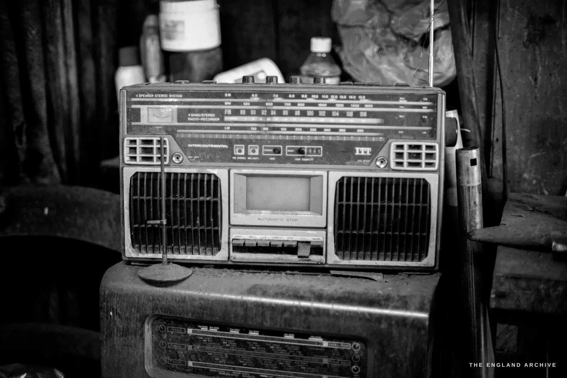 A vintage portable cassette radio perched on a grimy cabinet amid bottles and clutter, its dials and speaker grilles facing the room.