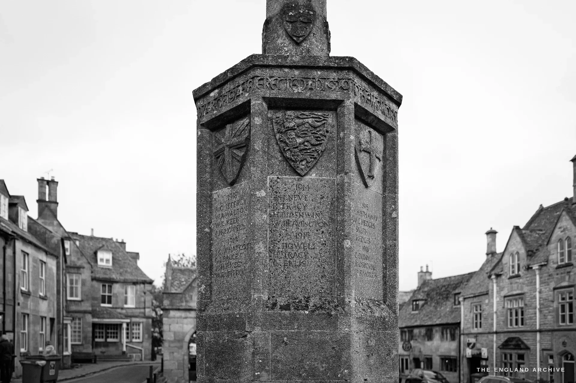 A frontal study of the carved octagonal monument, its heraldic shields and dense panels of inscribed names sharp, the street receding behind.