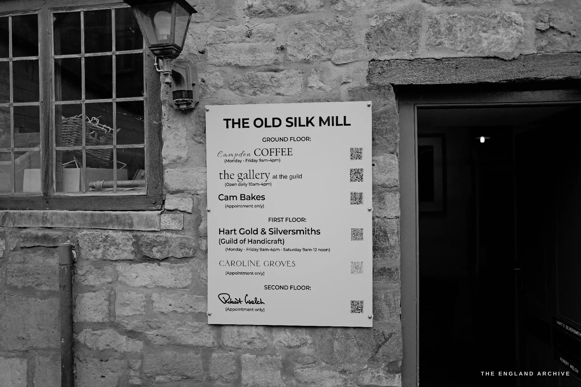 The white tenant directory of the Old Silk Mill beside the dark doorway, listing the businesses by floor - among them Hart Gold and Silversmiths - under an iron wall lantern.