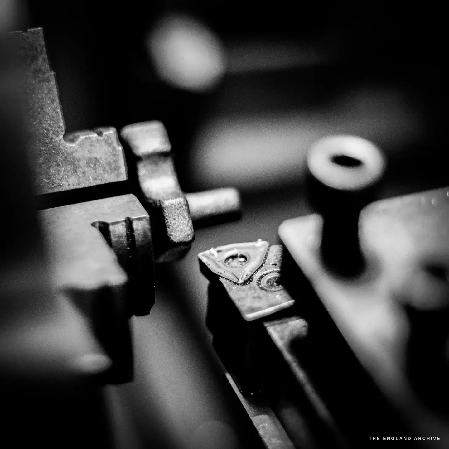A close, shallow-focus study of the lathe tooling - a hardened cutting tip clamped in a tool post, brass and blued steel behind.
