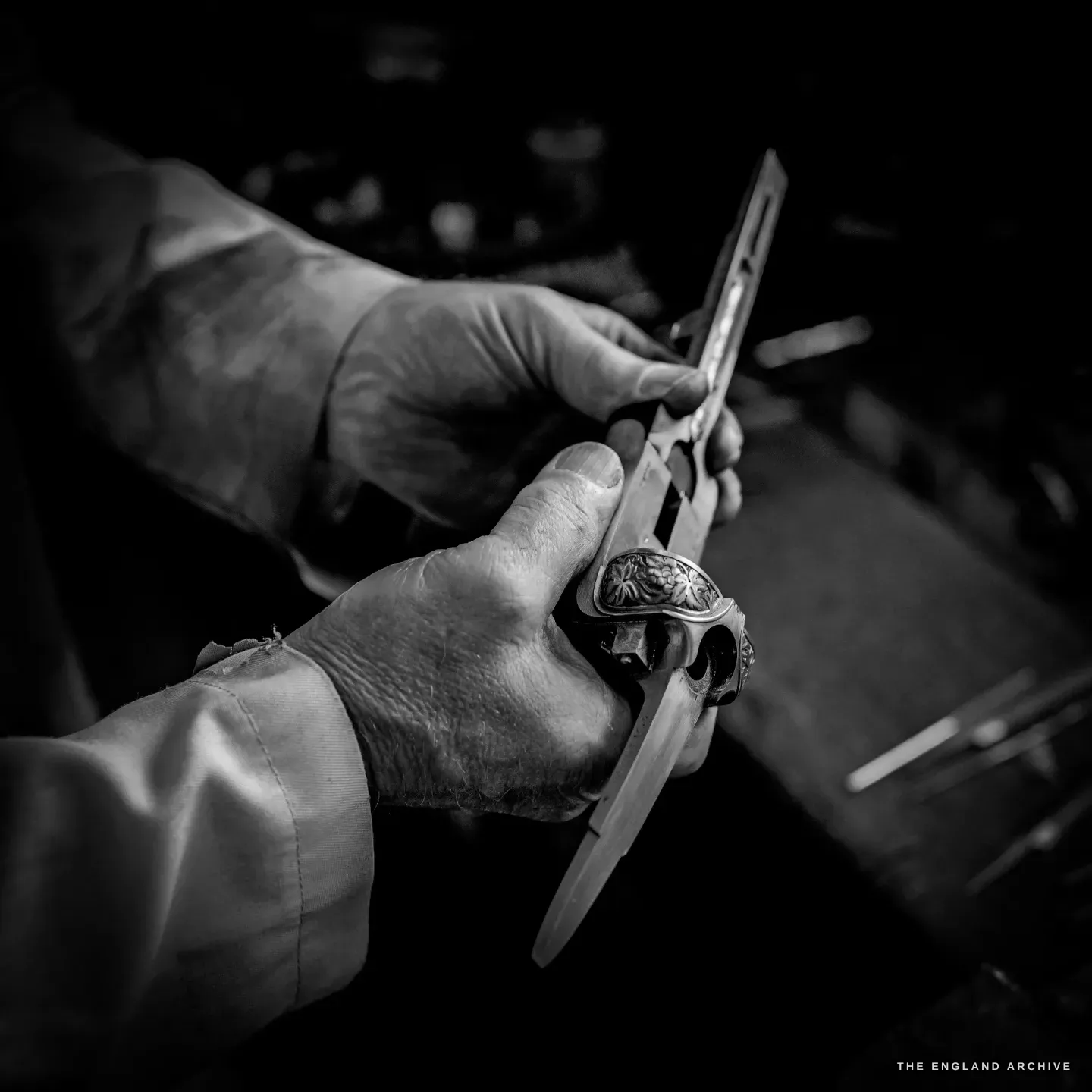 Haydn Hill's hand holds a small engraved gun part up to a measuring gauge, the fine scrollwork catching the light.